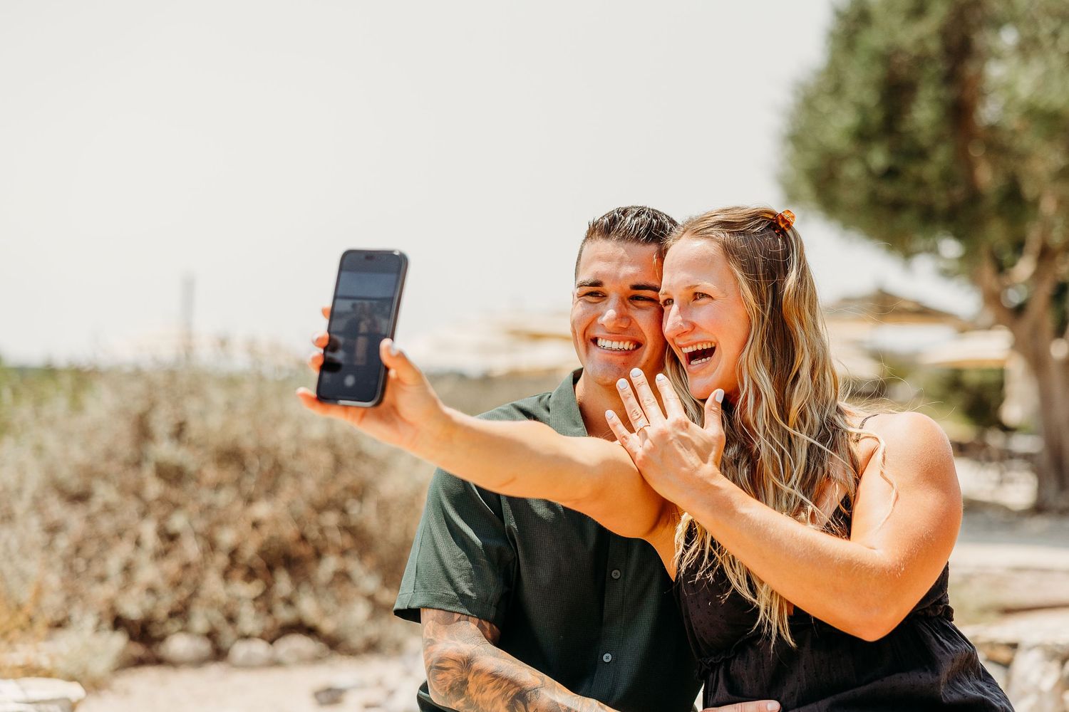 Two people taking a selfie together outdoors on a sunny day with smiles and laughter.