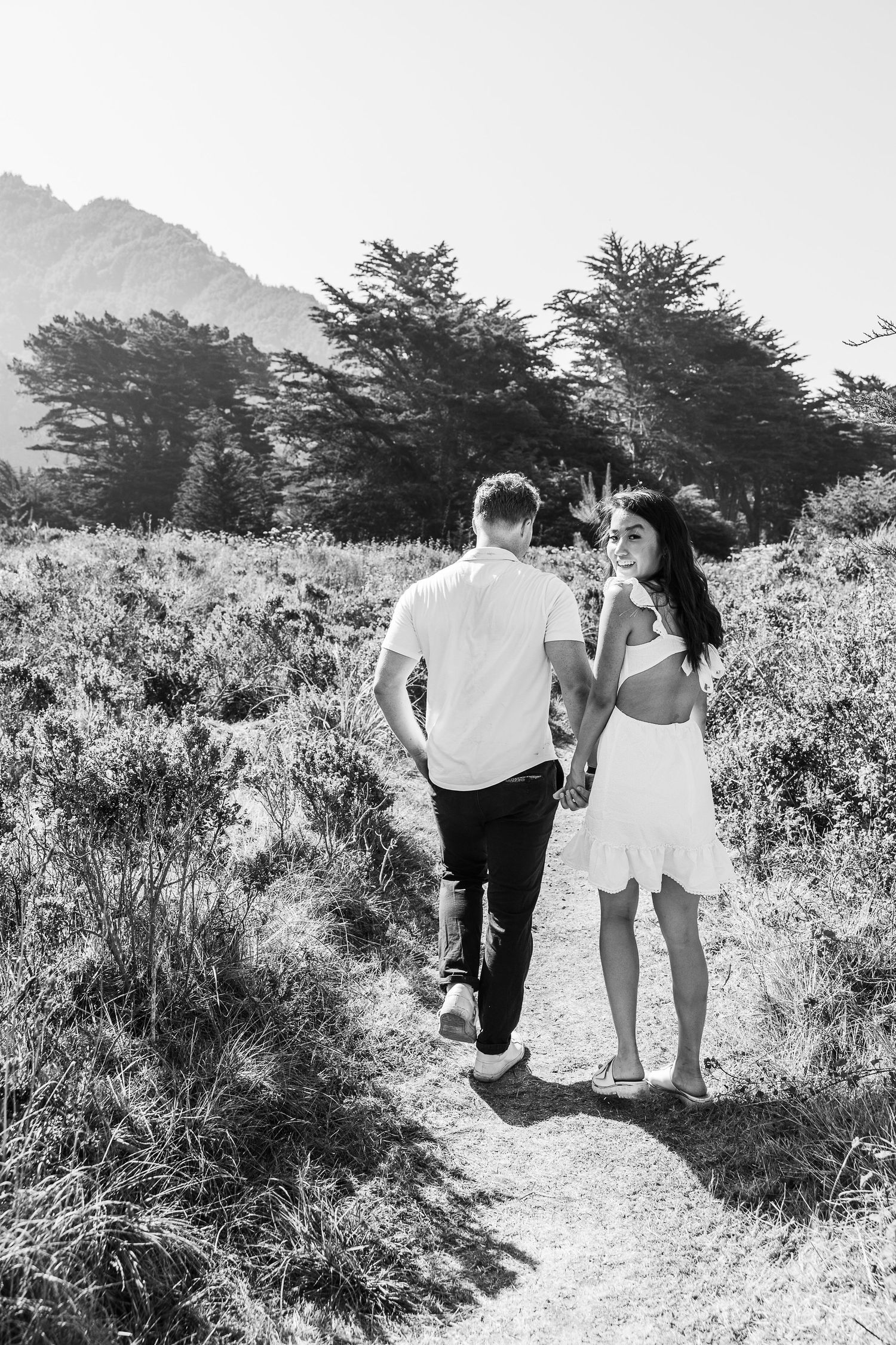 Black and white image of a couple walking together on a winding trail through nature.