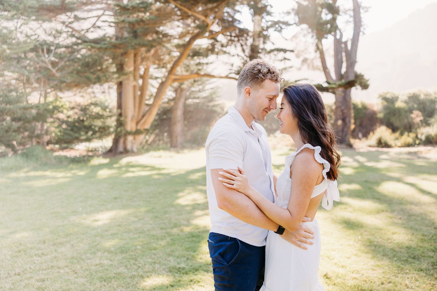 Couple in white and blue outfits sharing an intimate moment in a sunlit park.