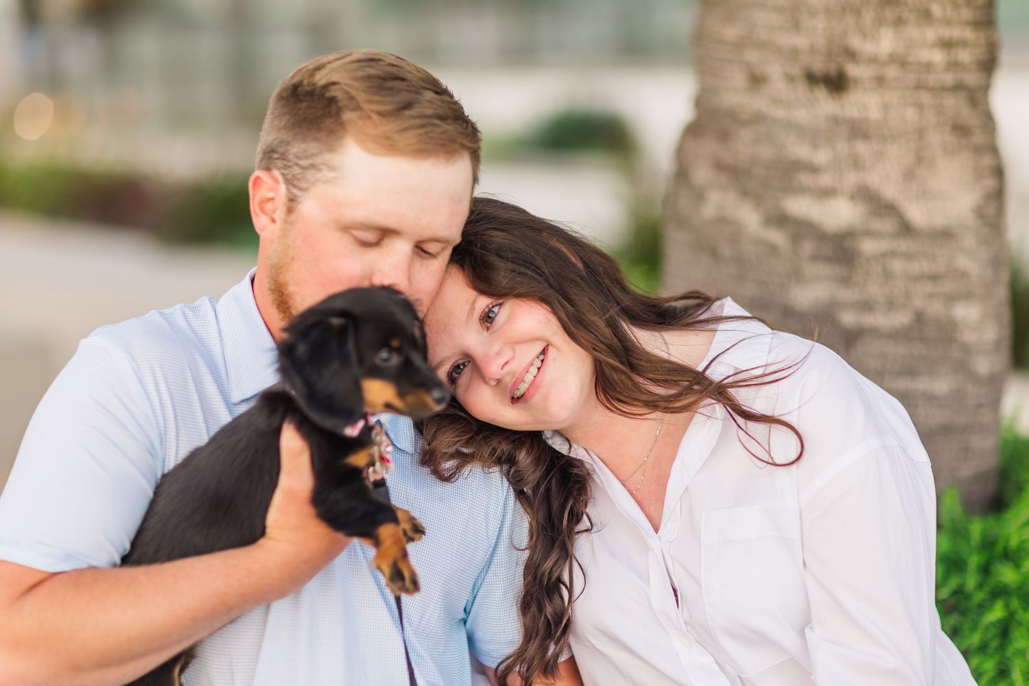 A loving couple cuddles with their small black puppy outdoors.