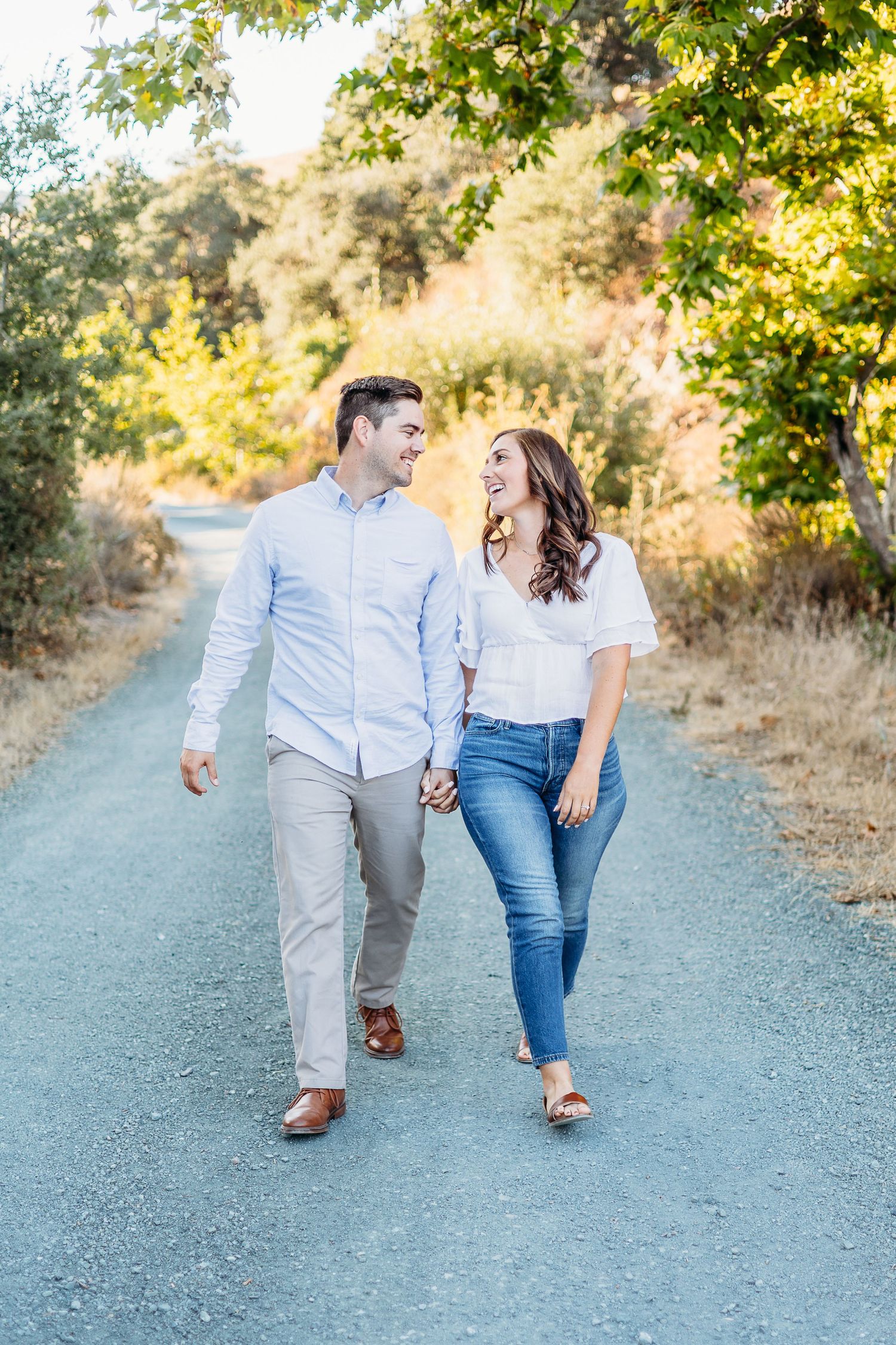 A couple shares laughter while strolling together on a gravel path in casual attire.