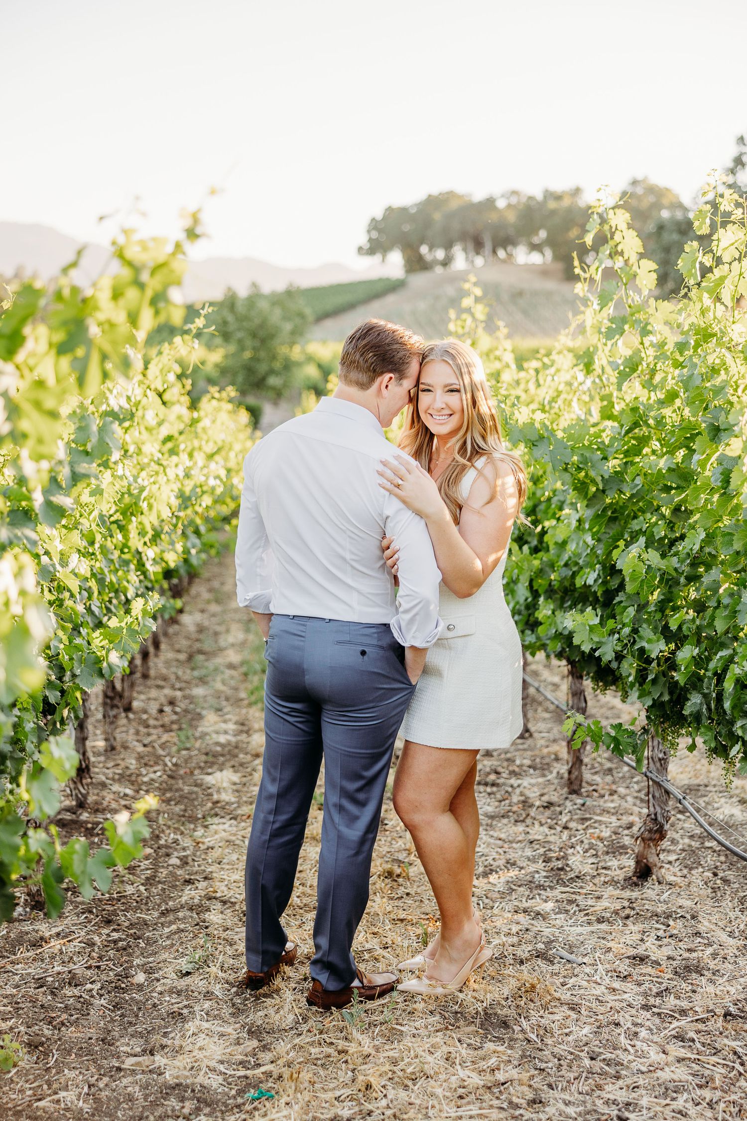 Romantic couple sharing intimate moment among vineyard rows during sunset photoshoot.