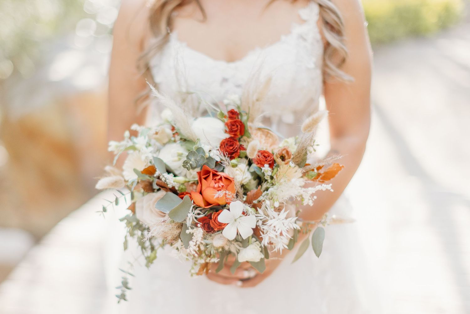 A bride holds a beautiful bouquet with coral and white flowers and cascading greenery against her white wedding dress.