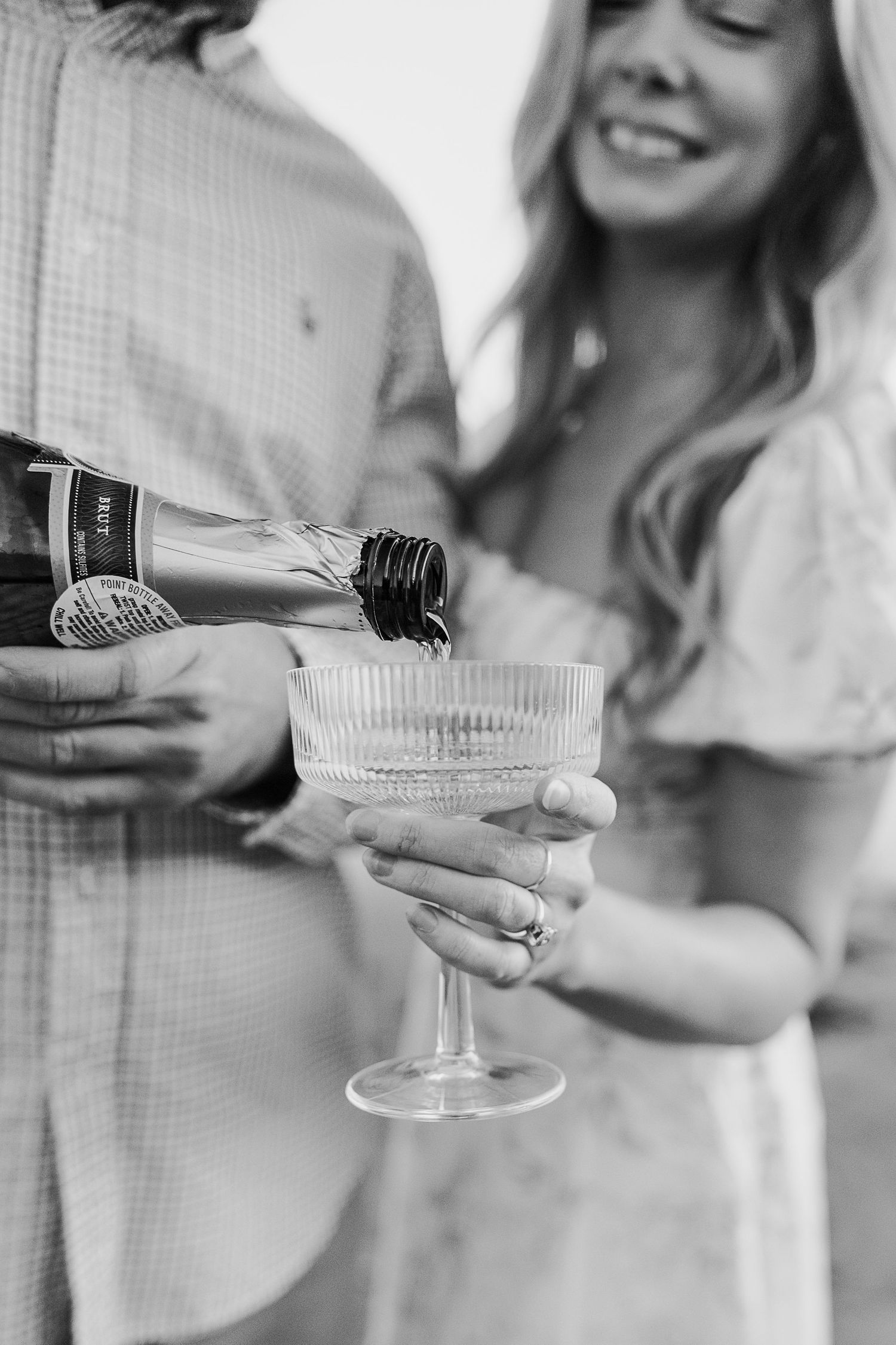 Black and white close-up of hands holding champagne glasses in celebratory toast.