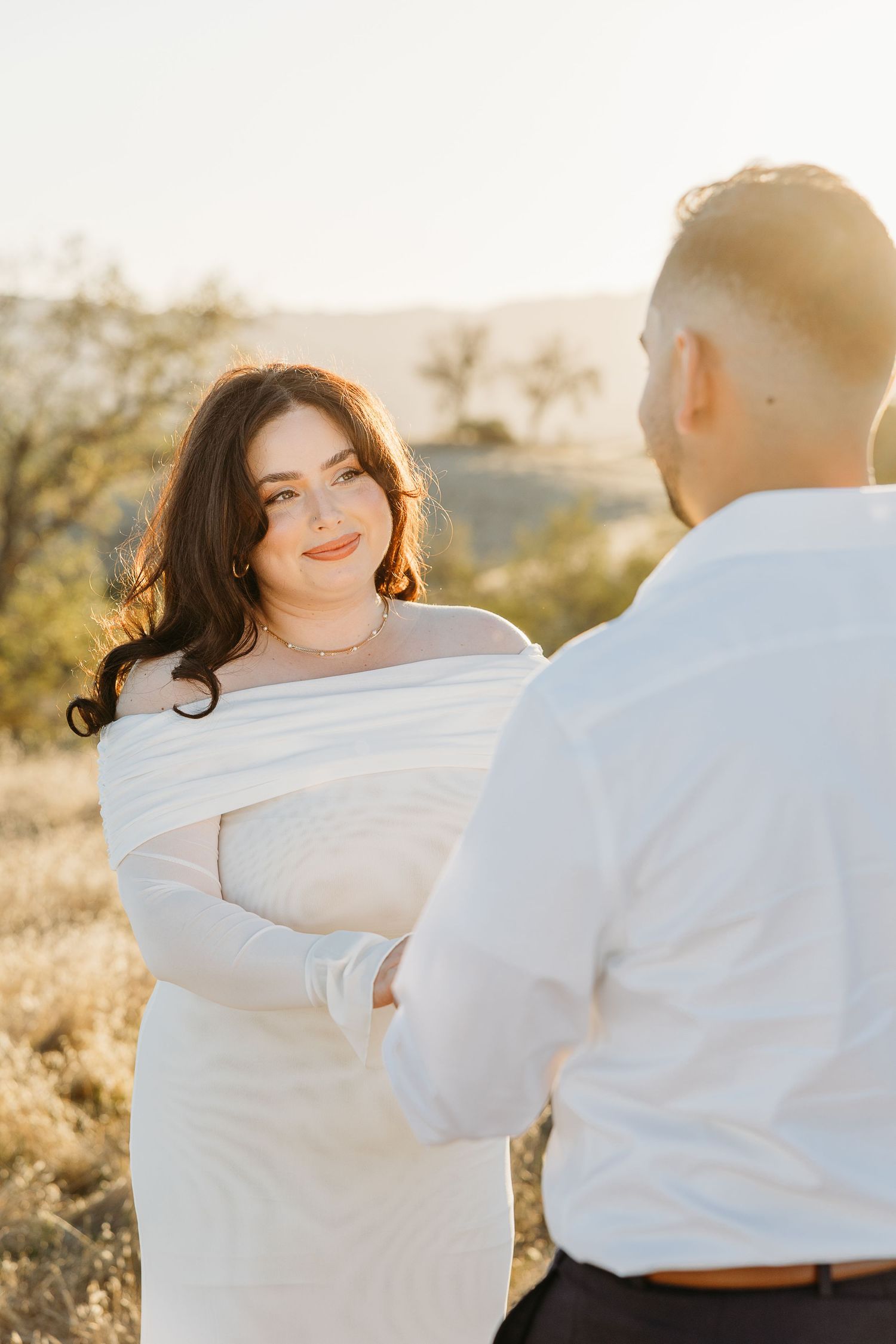 A romantic couple in white clothing shares intimate moments in a sun-drenched outdoor setting.