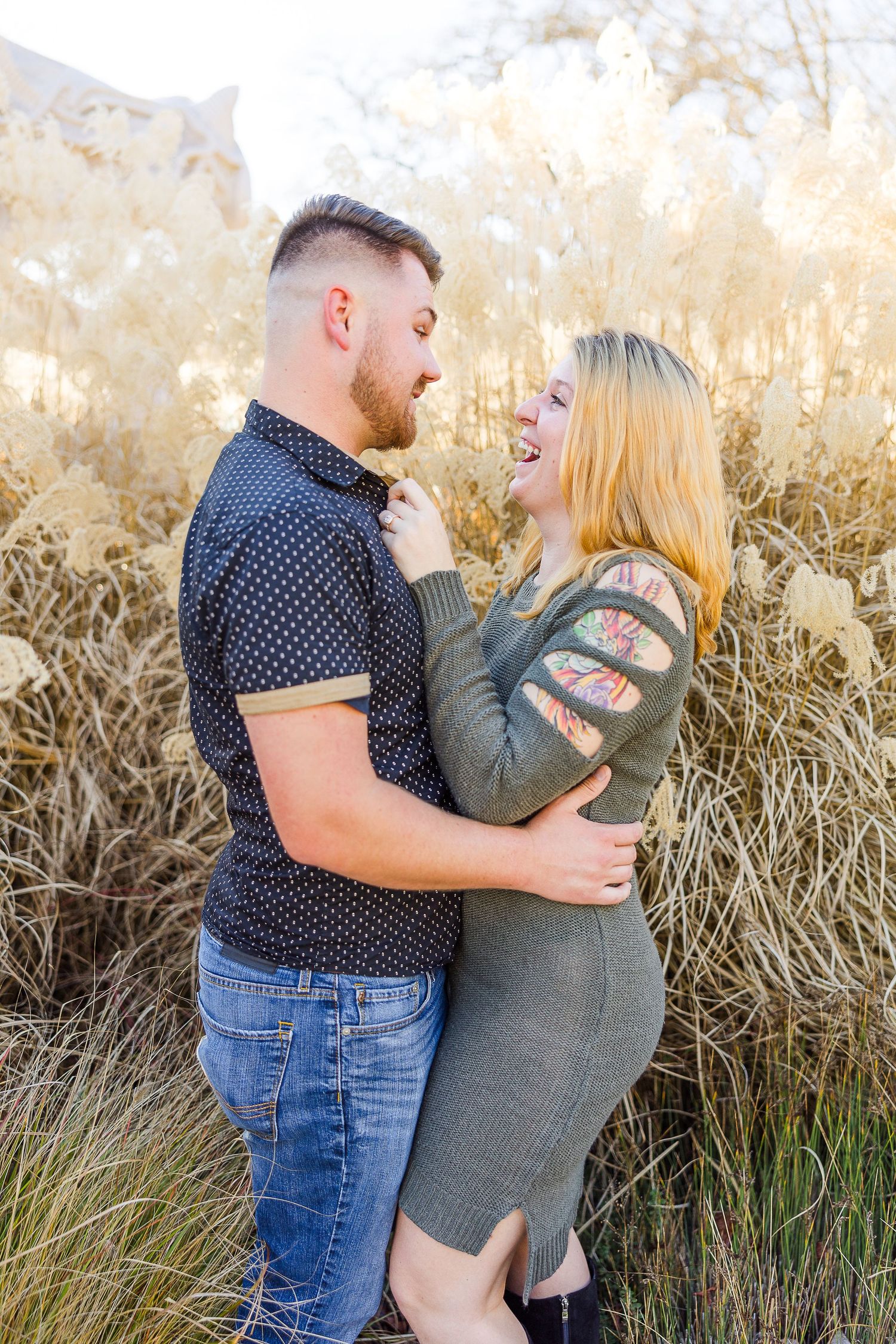 A couple embraces in front of tall golden grasses during a sunset photo shoot.