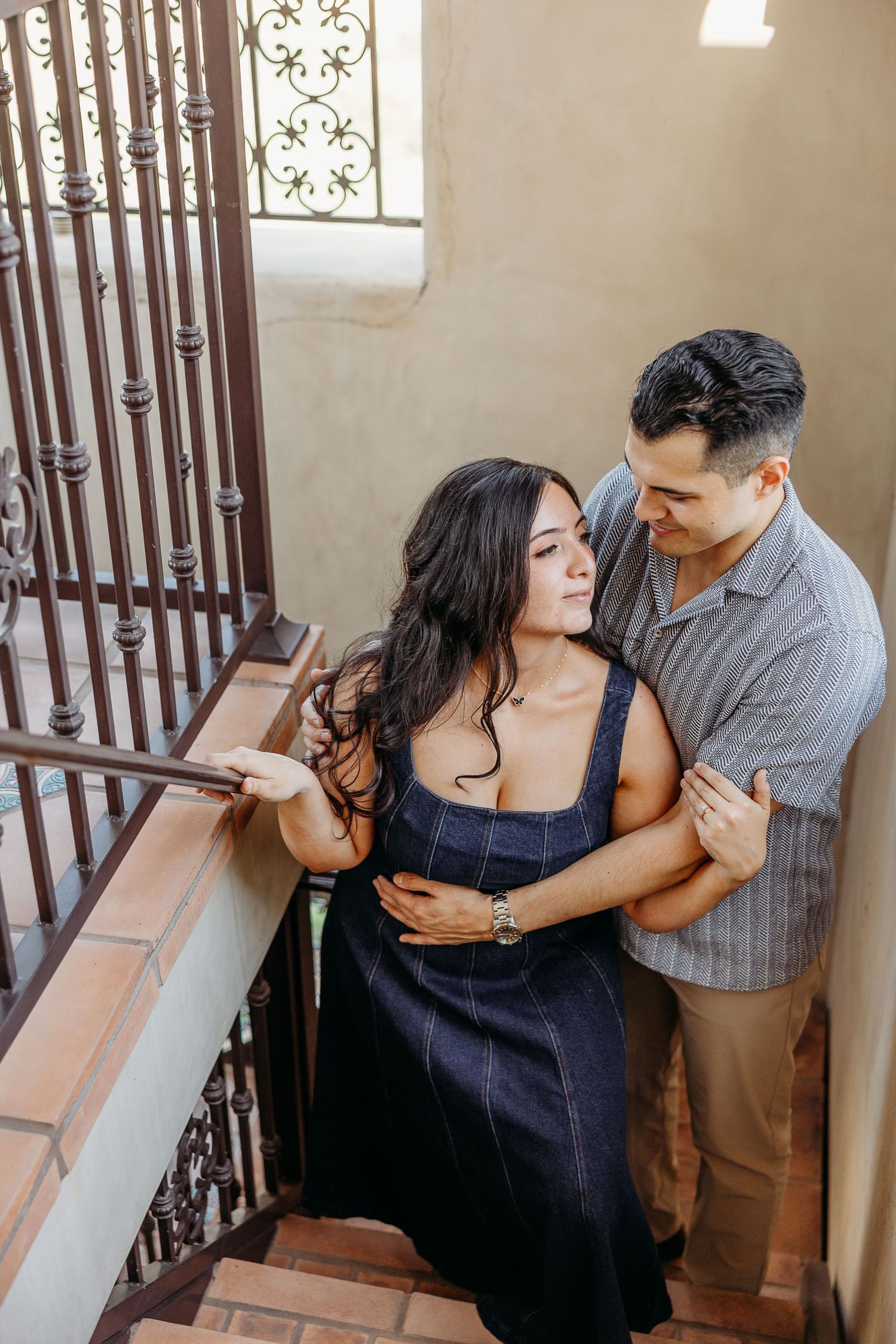 Couple sharing an intimate moment on a staircase with ornate iron railings.