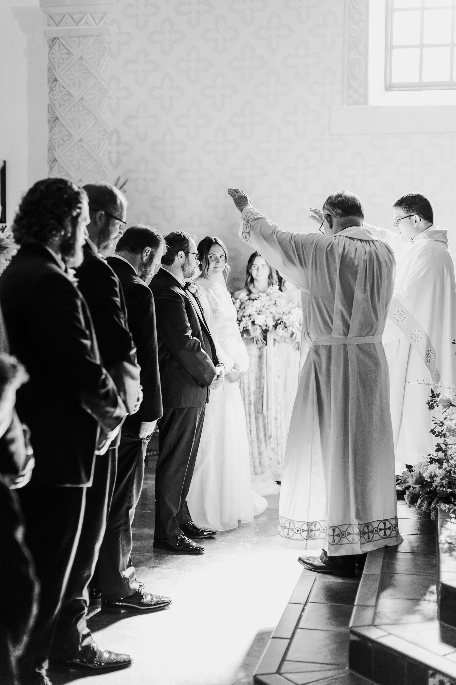A black and white photo of a religious wedding ceremony with the priest blessing the couple in Mission San Luis Obispo.