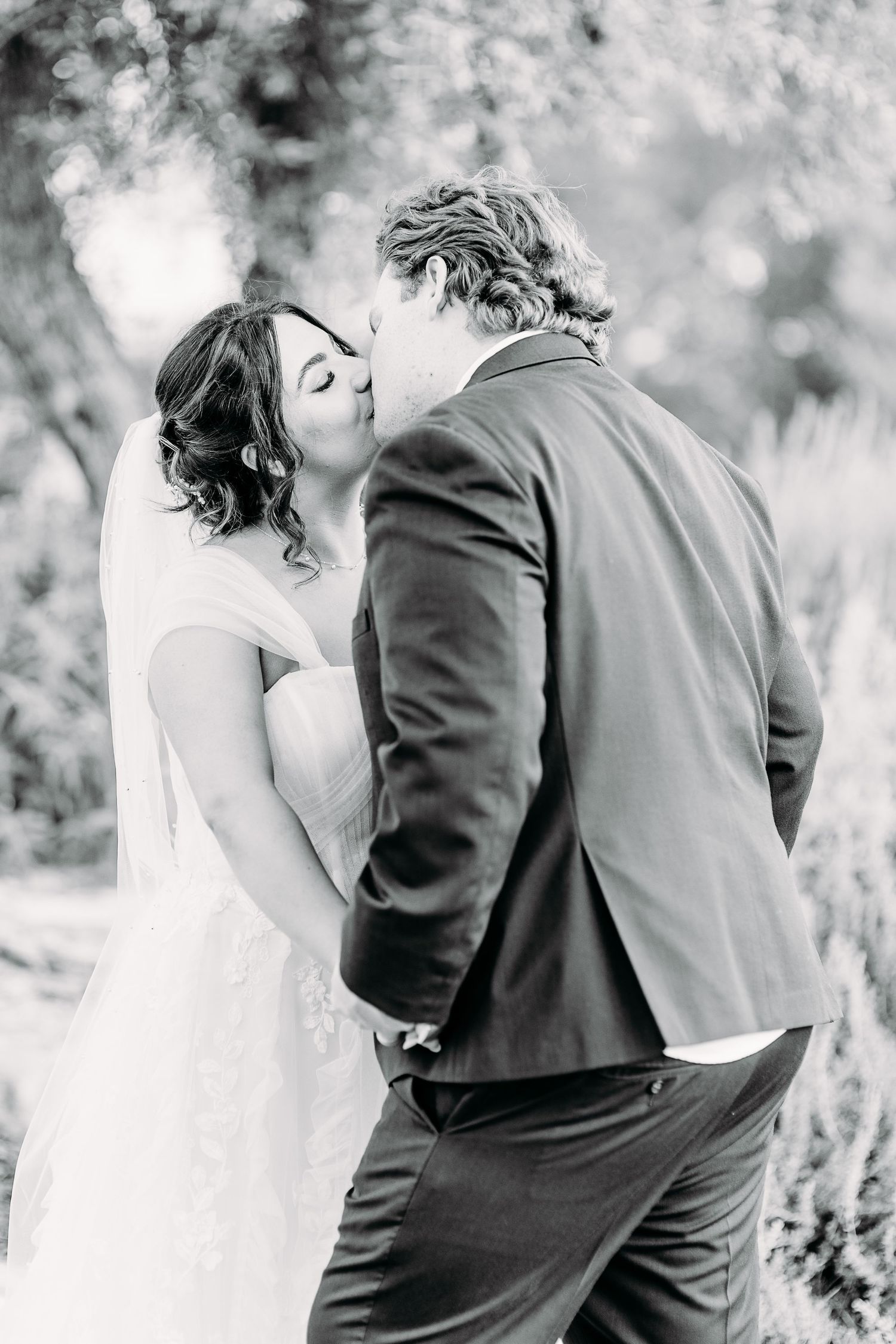 Black and white photo of a romantic first kiss between newlyweds in a beautiful outdoor setting.