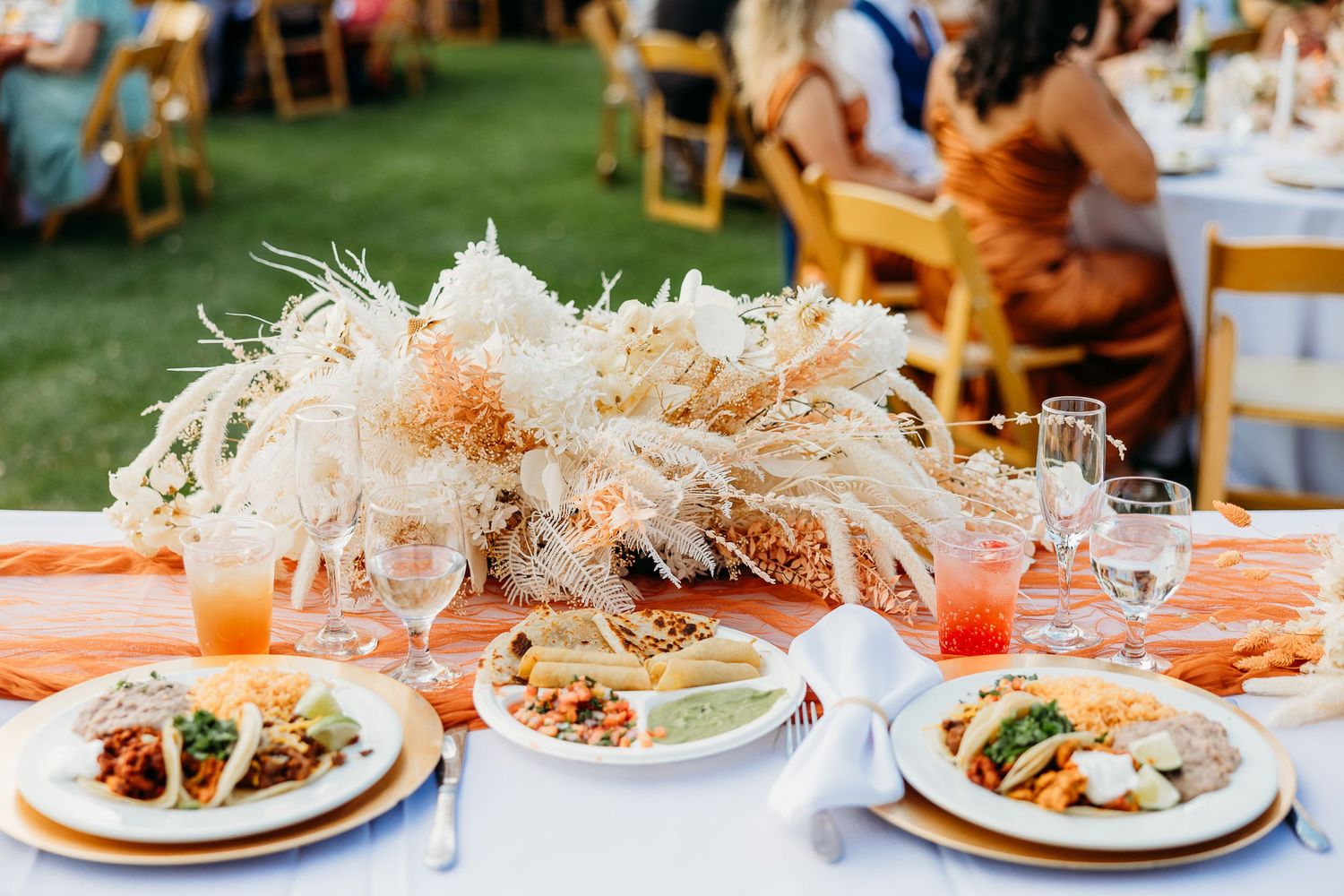 Wedding reception table settings with orange linens and Mexican food plates served outdoors.