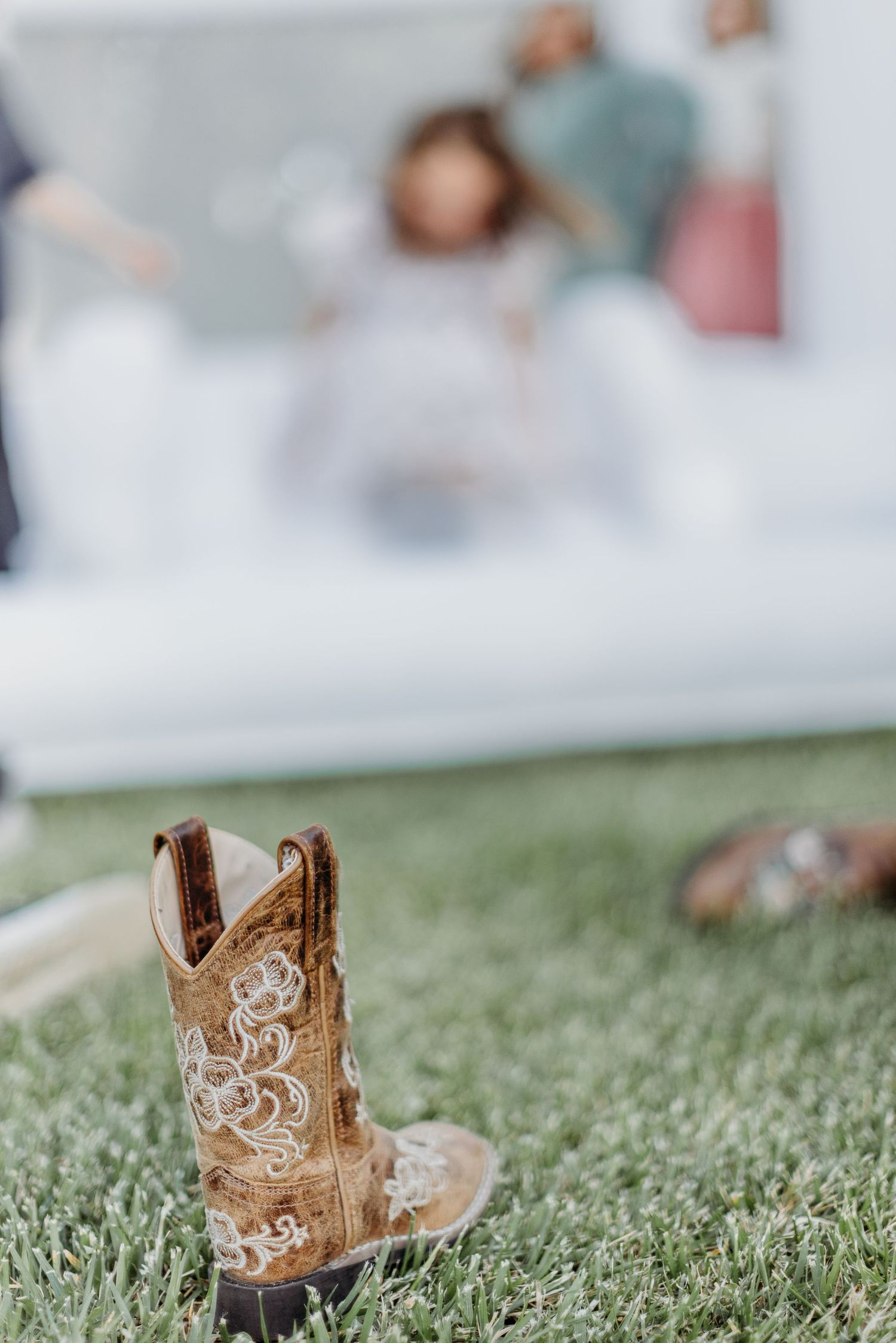 Decorative brown leather cowboy boots with intricate embroidery sitting on green grass.