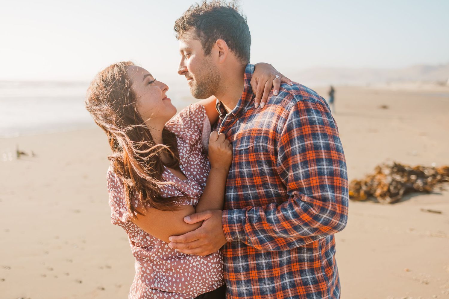 A couple embraces on a sandy beach during golden hour.