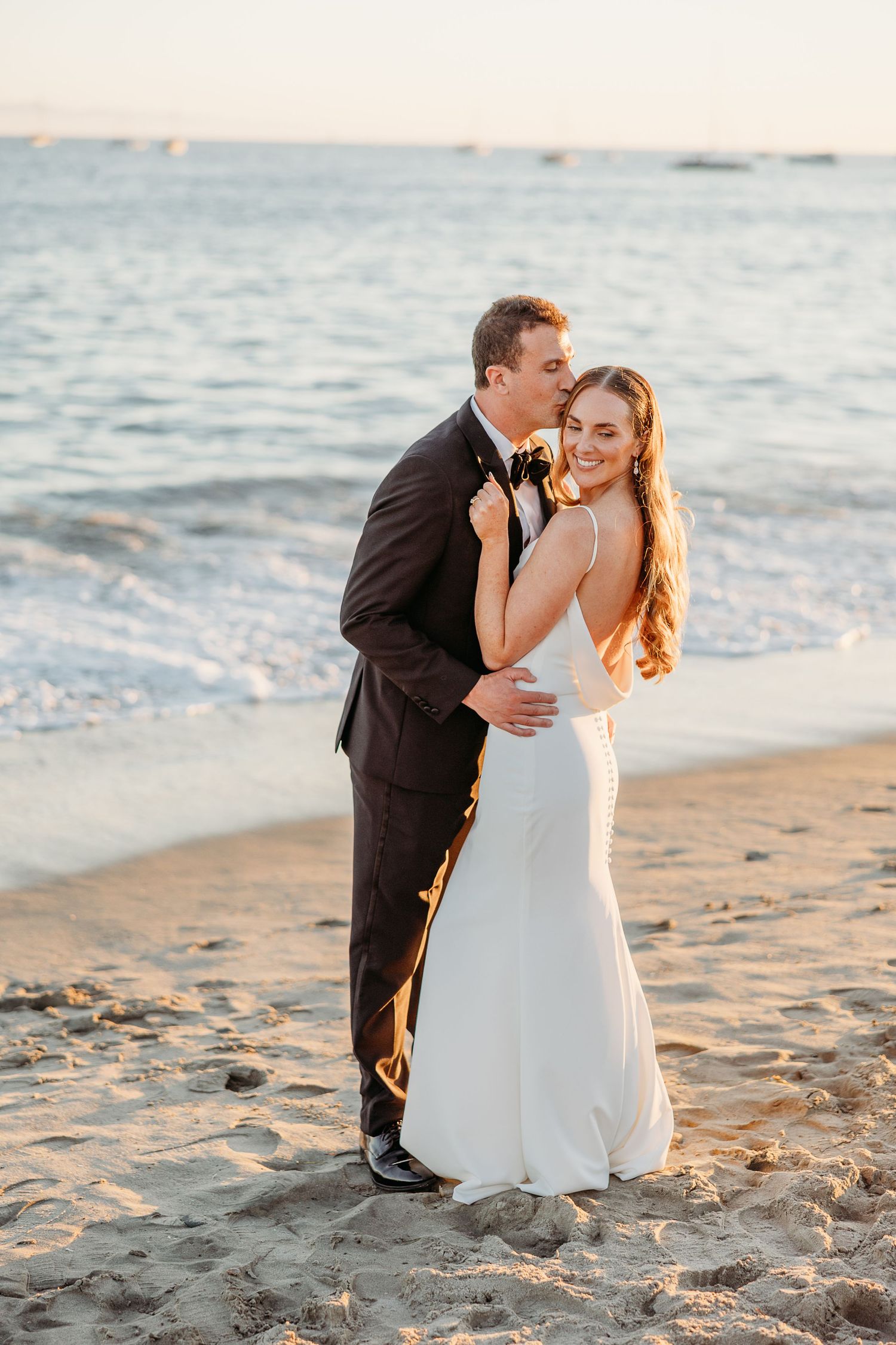 Romantic beach photoshoot of newlyweds at sunset with ocean waves in background.