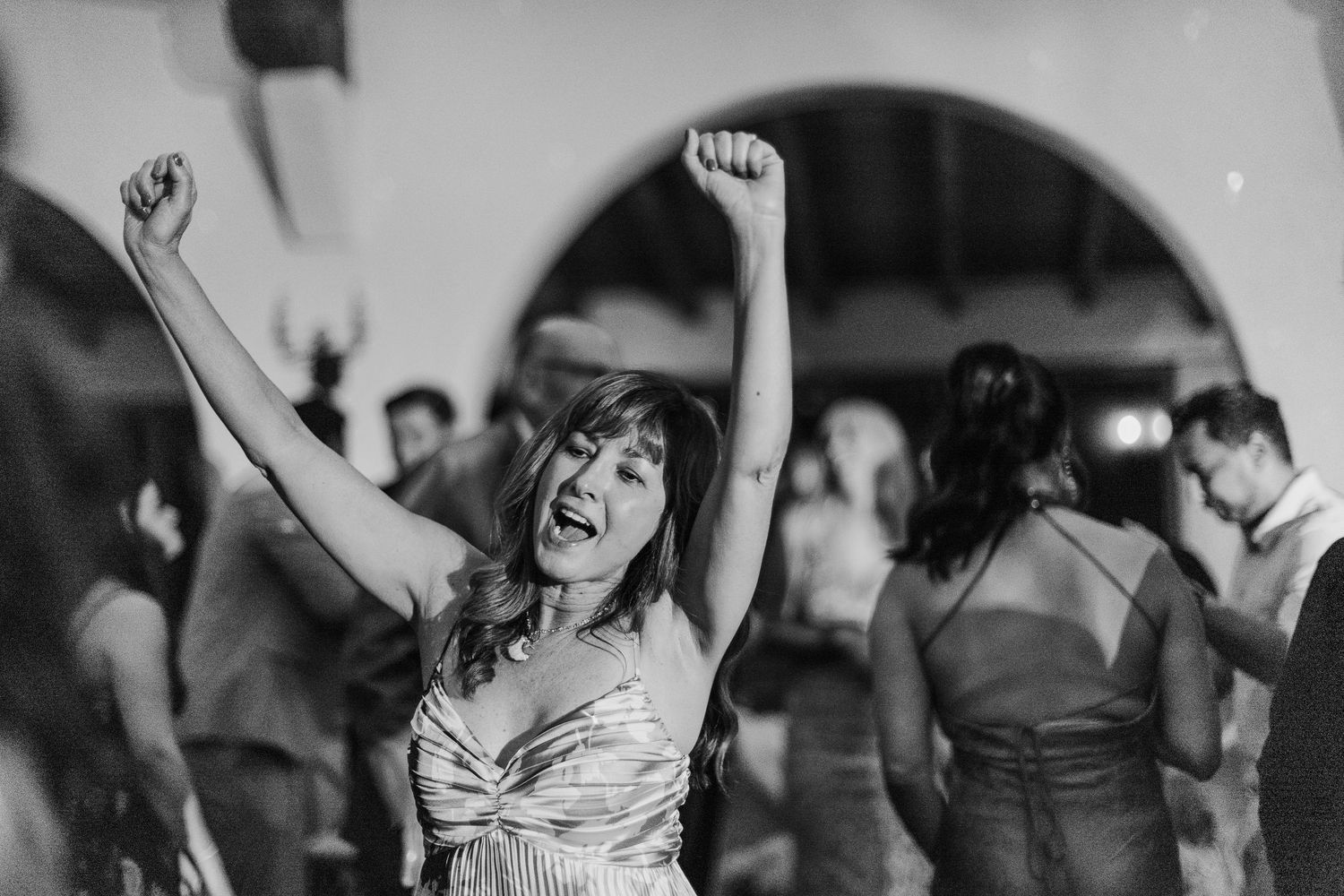 Black and white photo series of wedding guests dancing and celebrating with raised arms on a dance floor.