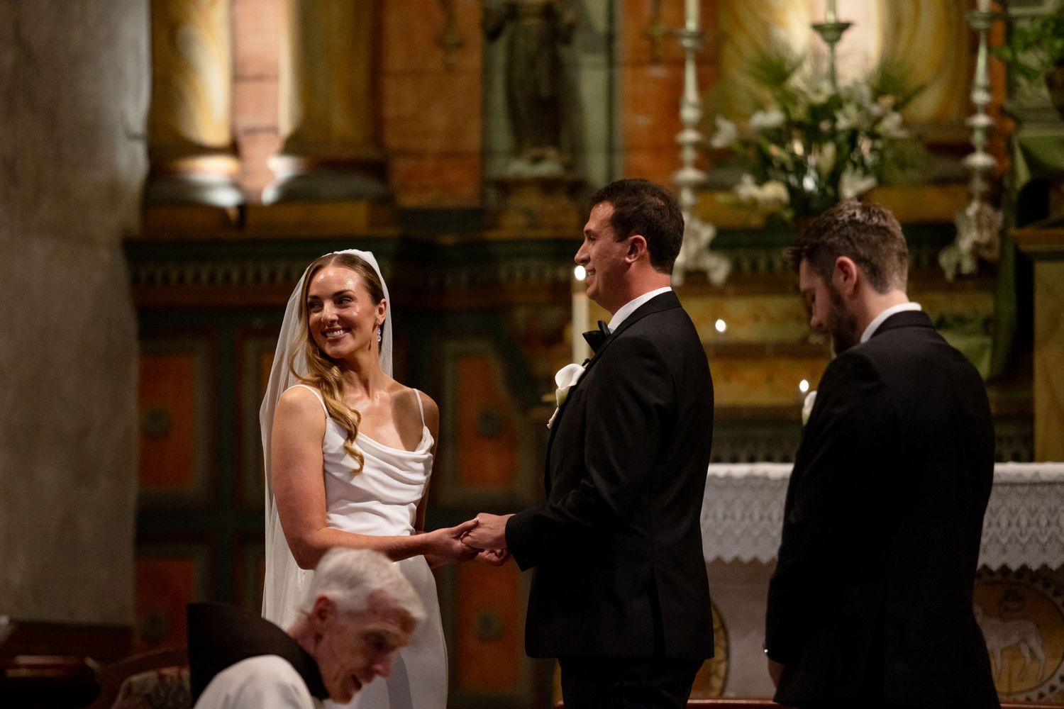 A wedding ceremony takes place inside a beautiful historic church with ornate decorations and lighting.