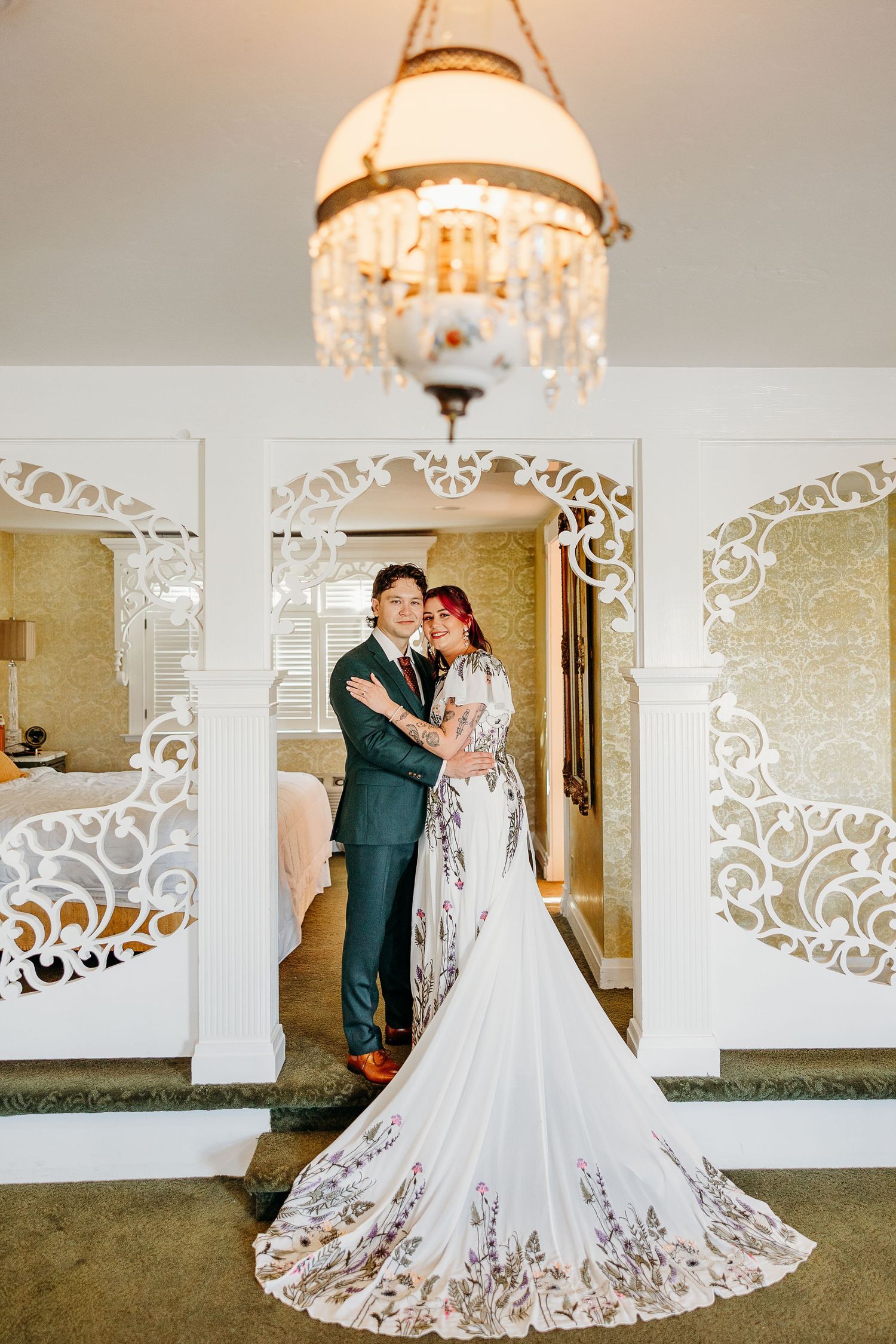 Elegant wedding couple dances in a luxurious venue with ornate white decorative screens and crystal chandeliers.