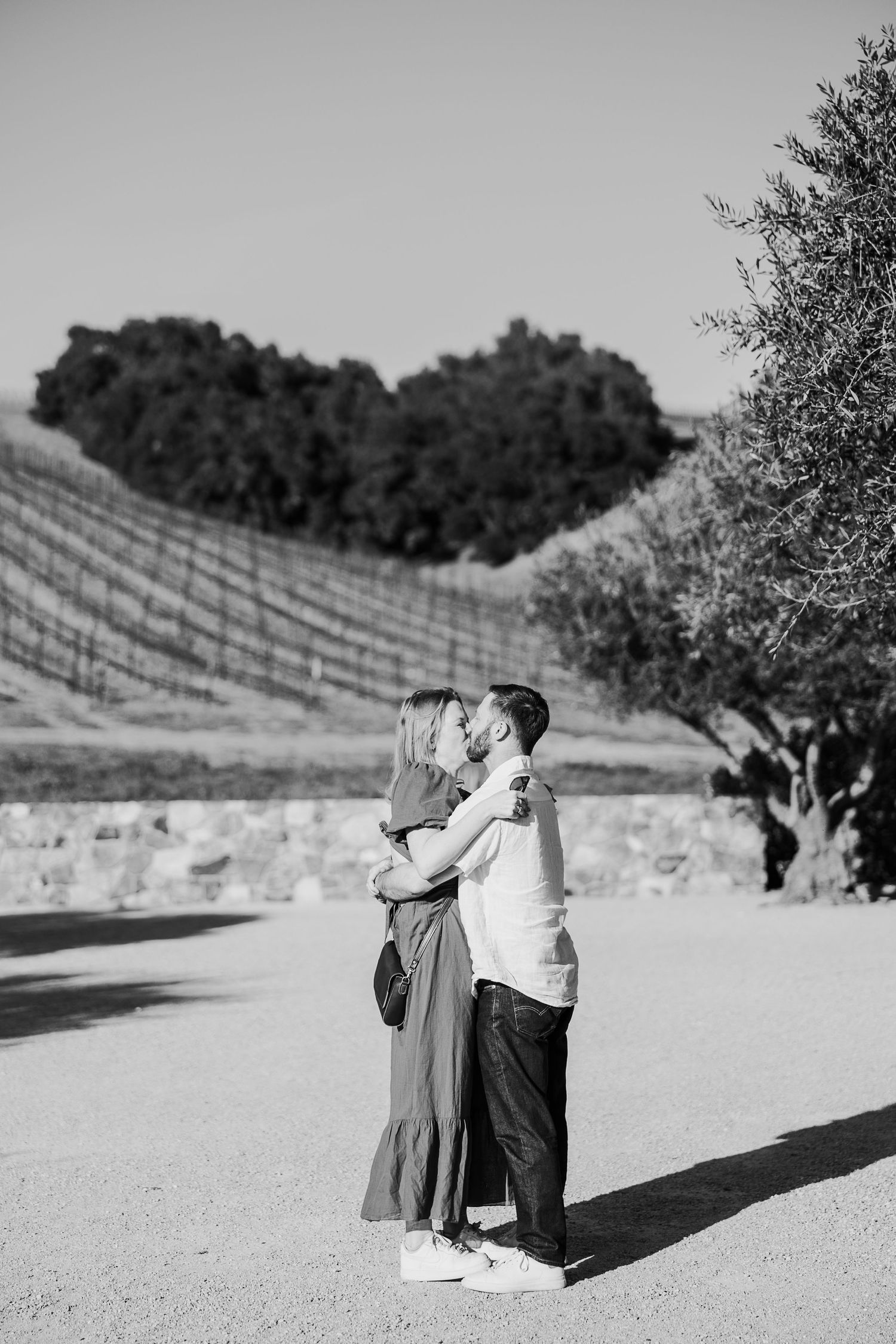 A couple shares a romantic moment in black and white against a scenic vineyard backdrop.