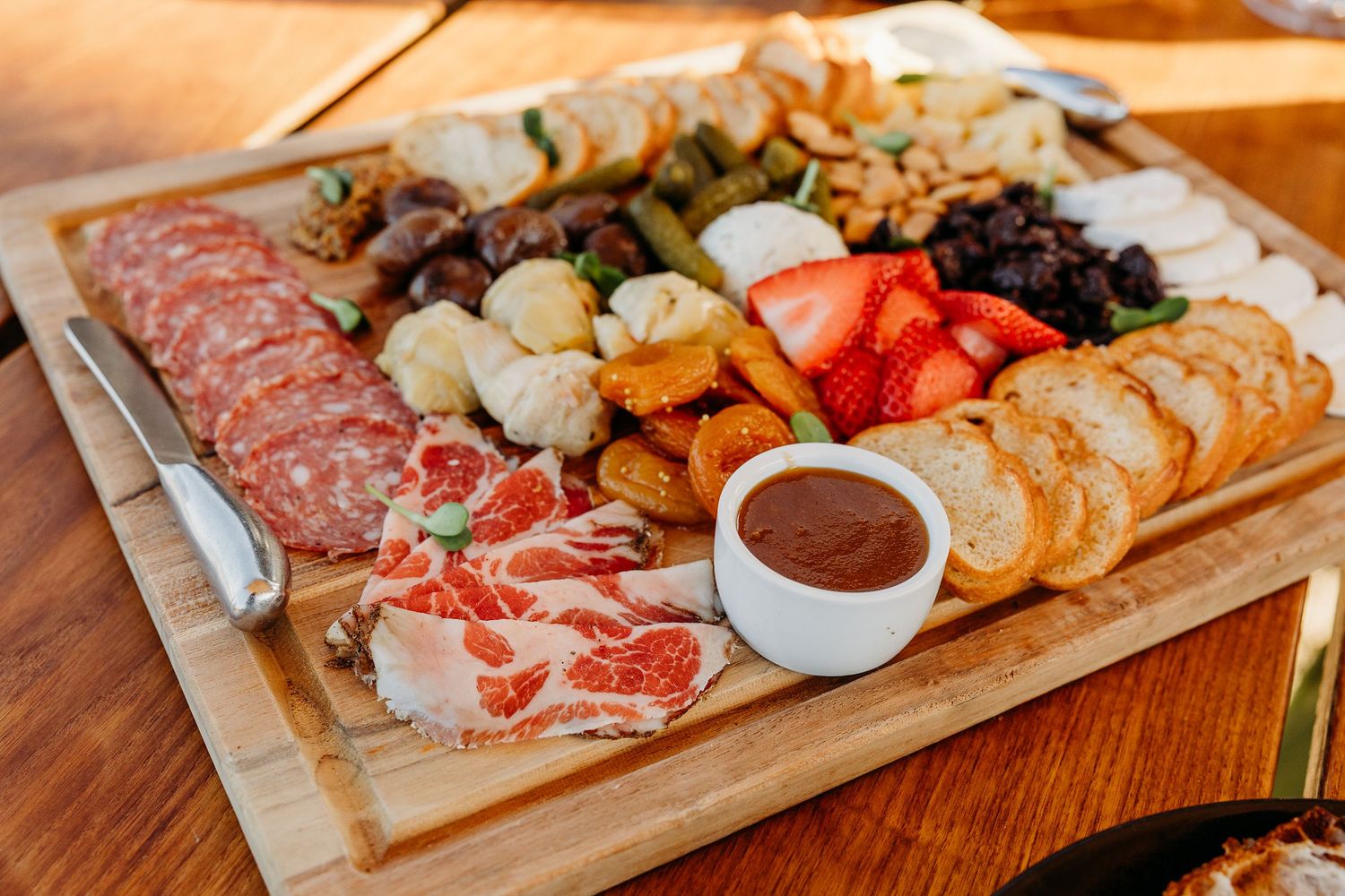Charcuterie board with meats, cheeses, and fruits arranged on wooden serving plank.