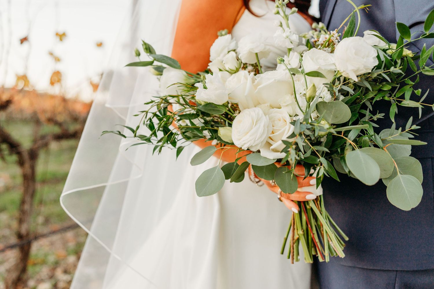 An elegant white wedding bouquet with roses and greenery against a navy suit.