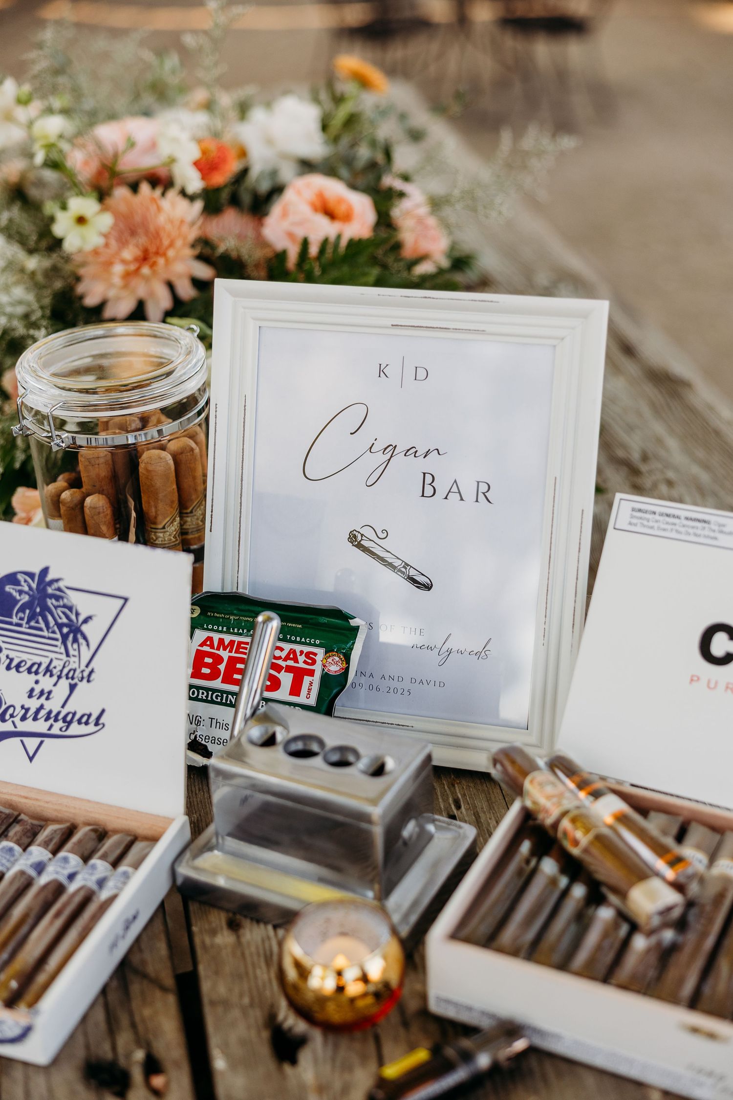 Elegant wedding cigar bar display with handwritten signs and various cigars arranged on wooden surfaces.