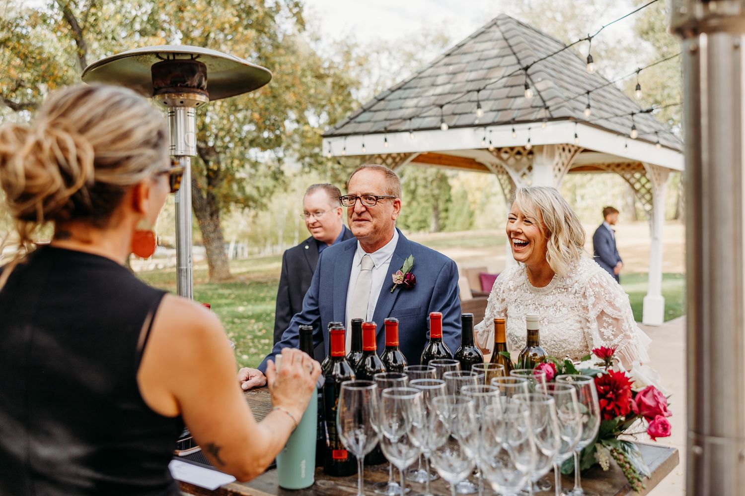 Wedding reception setup with elegant glassware and wine bottles on rustic tables.