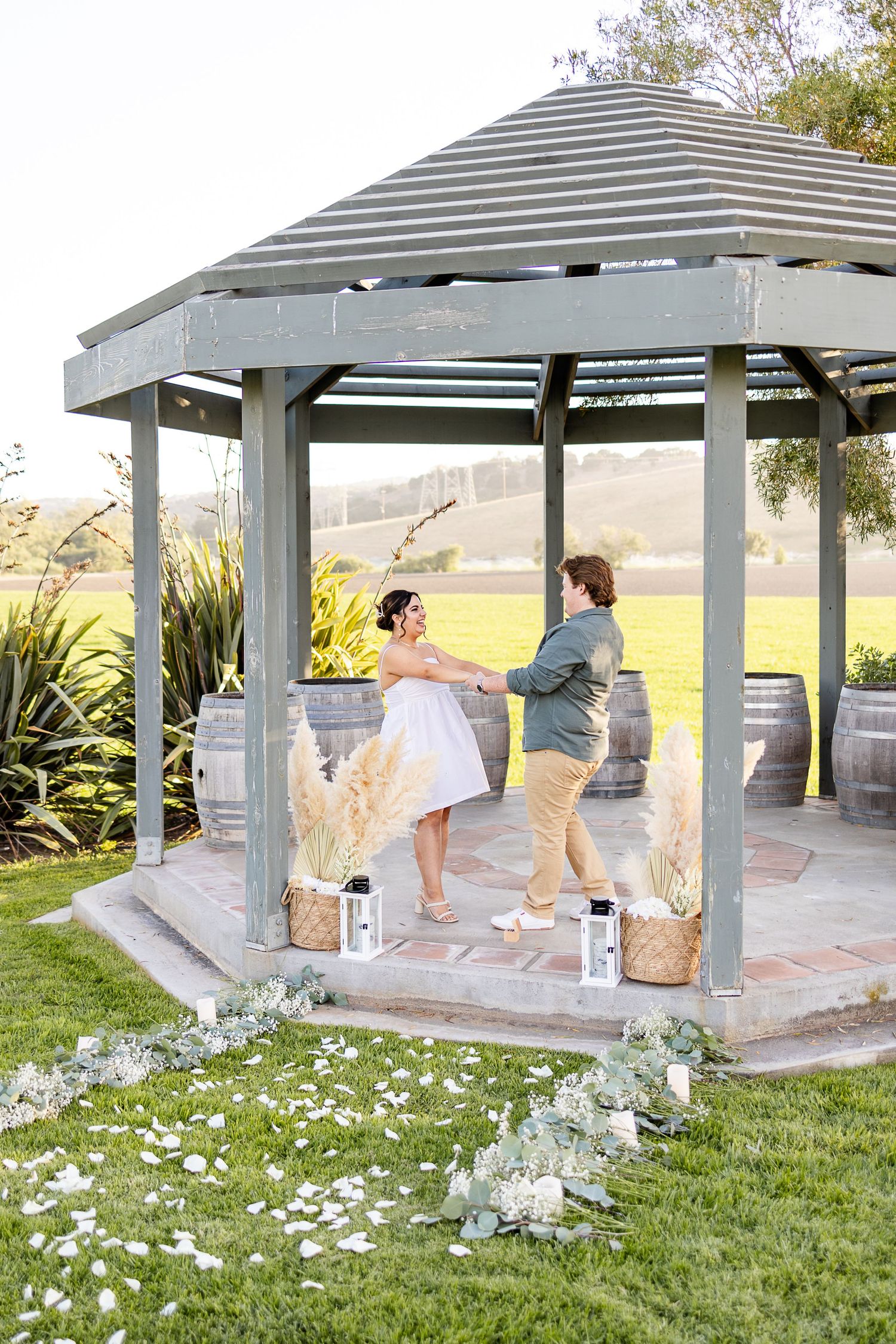 A playful interaction between two people in a gazebo surrounded by white flowers and greenery.