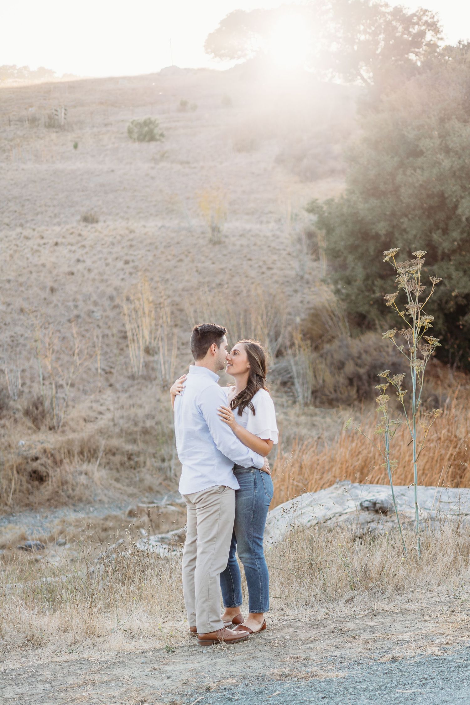 A romantic moment shared between a couple on a hillside path at sunset.