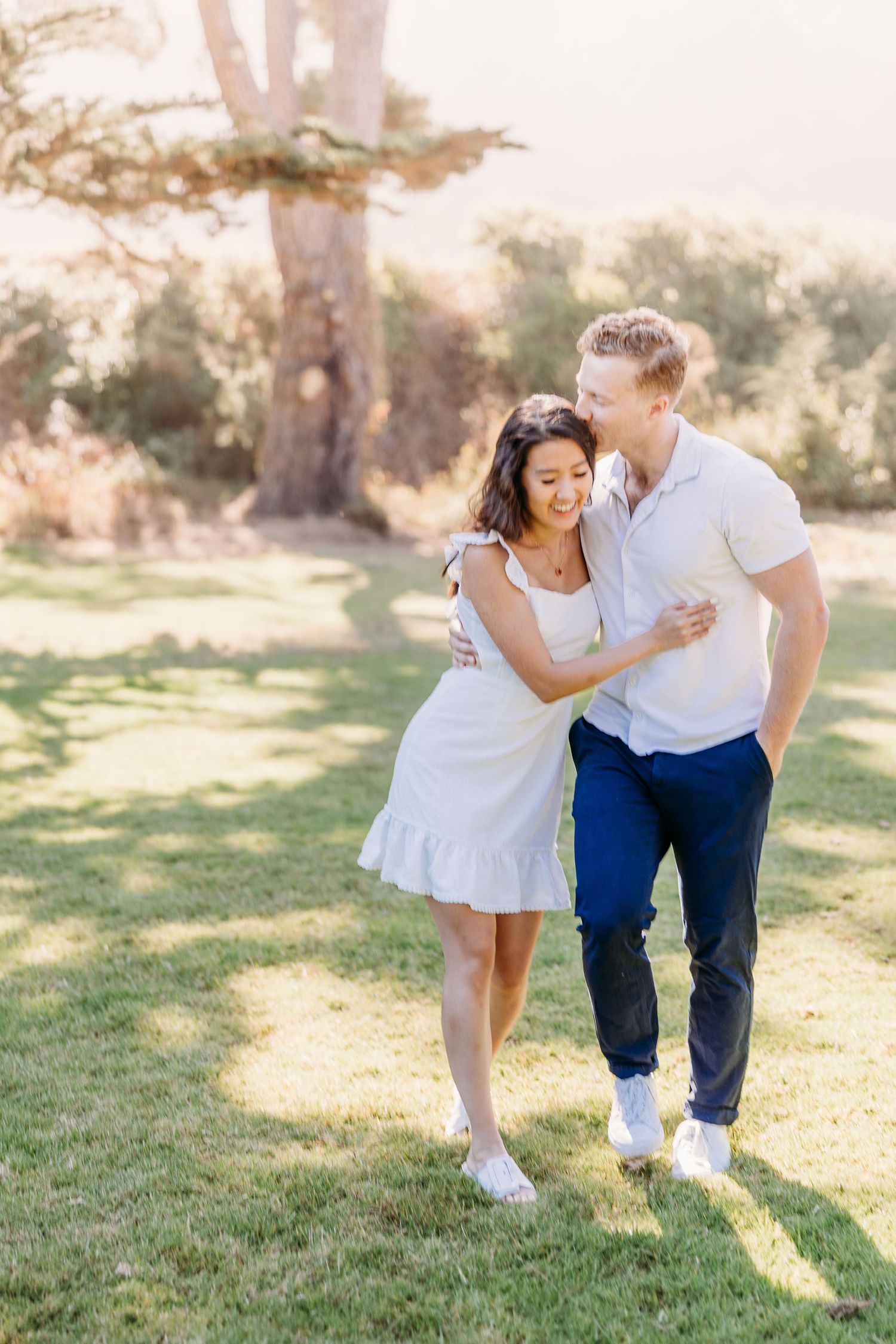 A couple shares a joyful moment together outdoors on a sunny day wearing white and blue casual attire.
