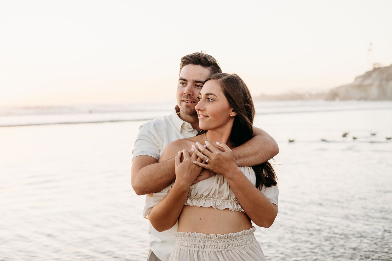 Joyful couple hugging and laughing together on beach during sunset.