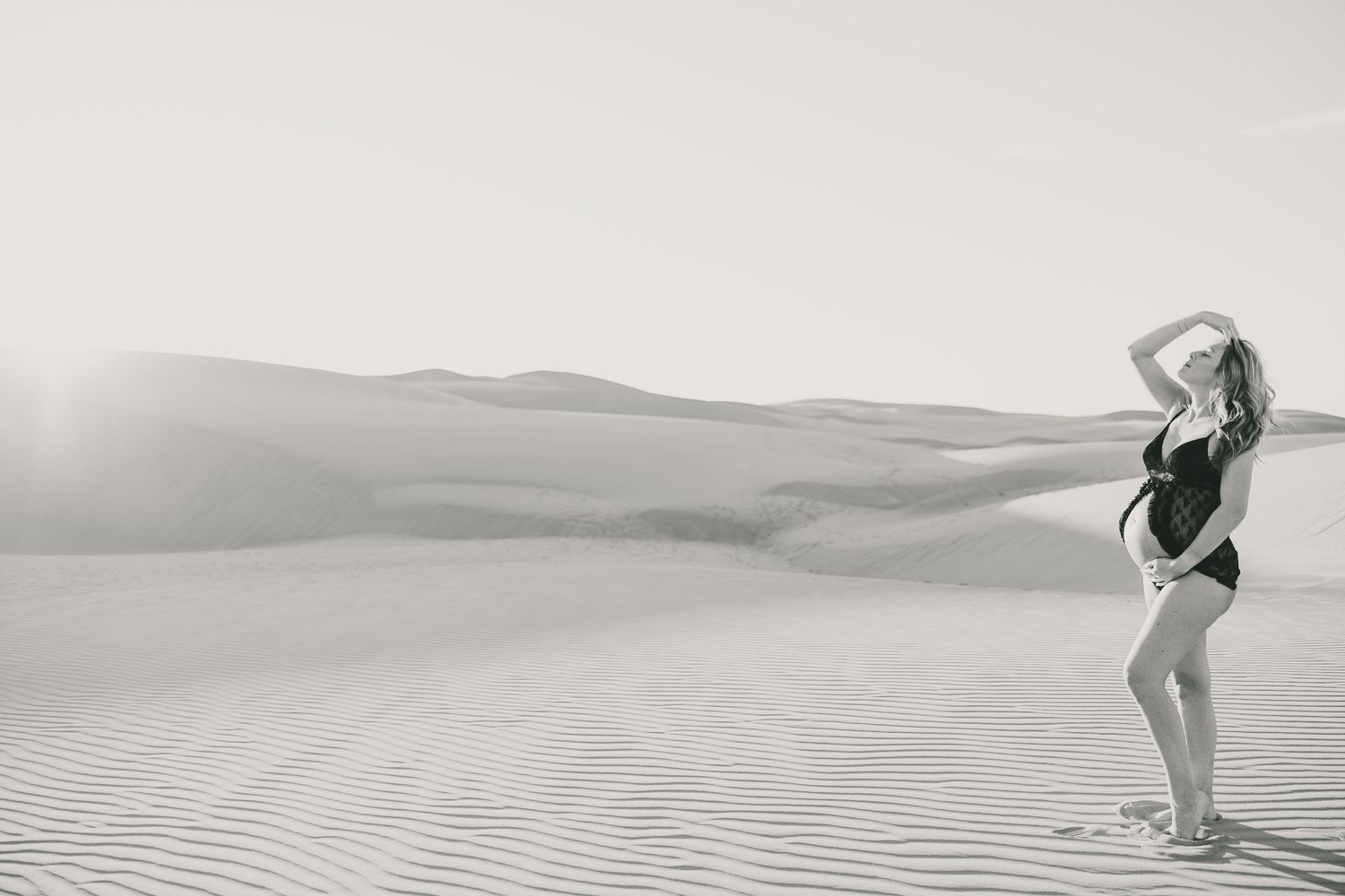 Black and white artistic desert maternity photo with dramatic pose.