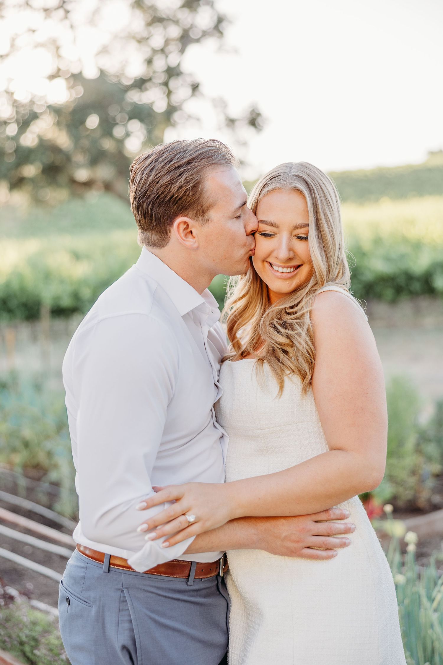 A romantic couple shares tender moments in an outdoor garden setting during a photo session at sunset.