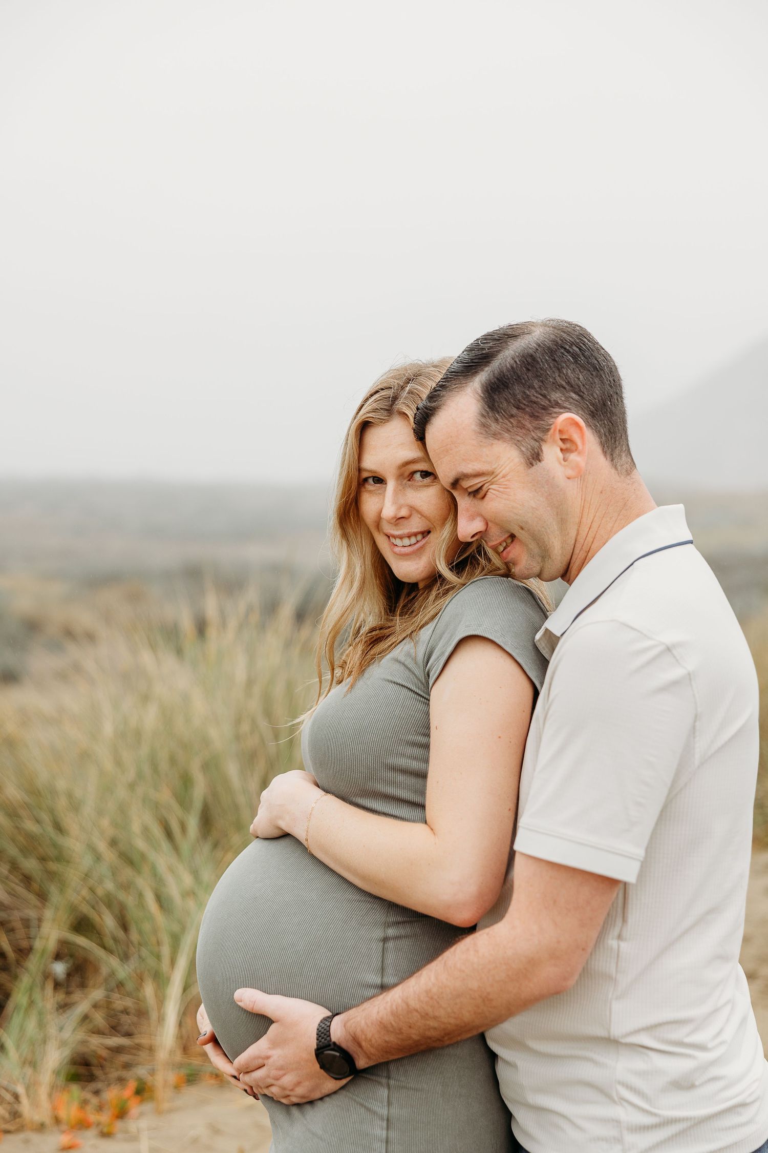 Sweet couple's maternity photo with scenic natural backdrop and coastal grasses.