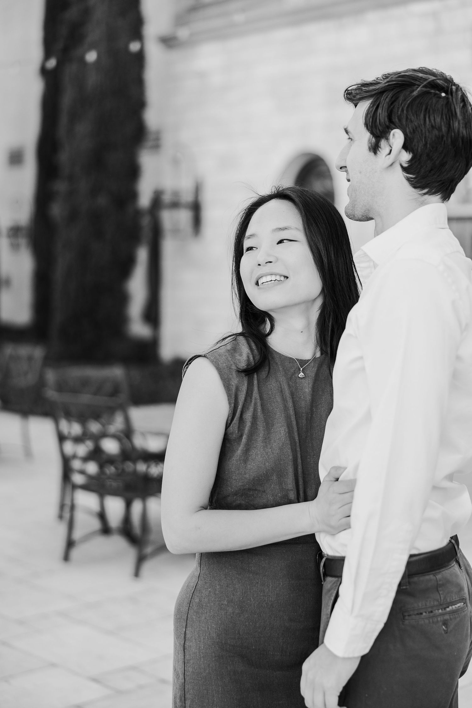 Black and white candid photo of a couple sharing a joyful moment together outdoors.