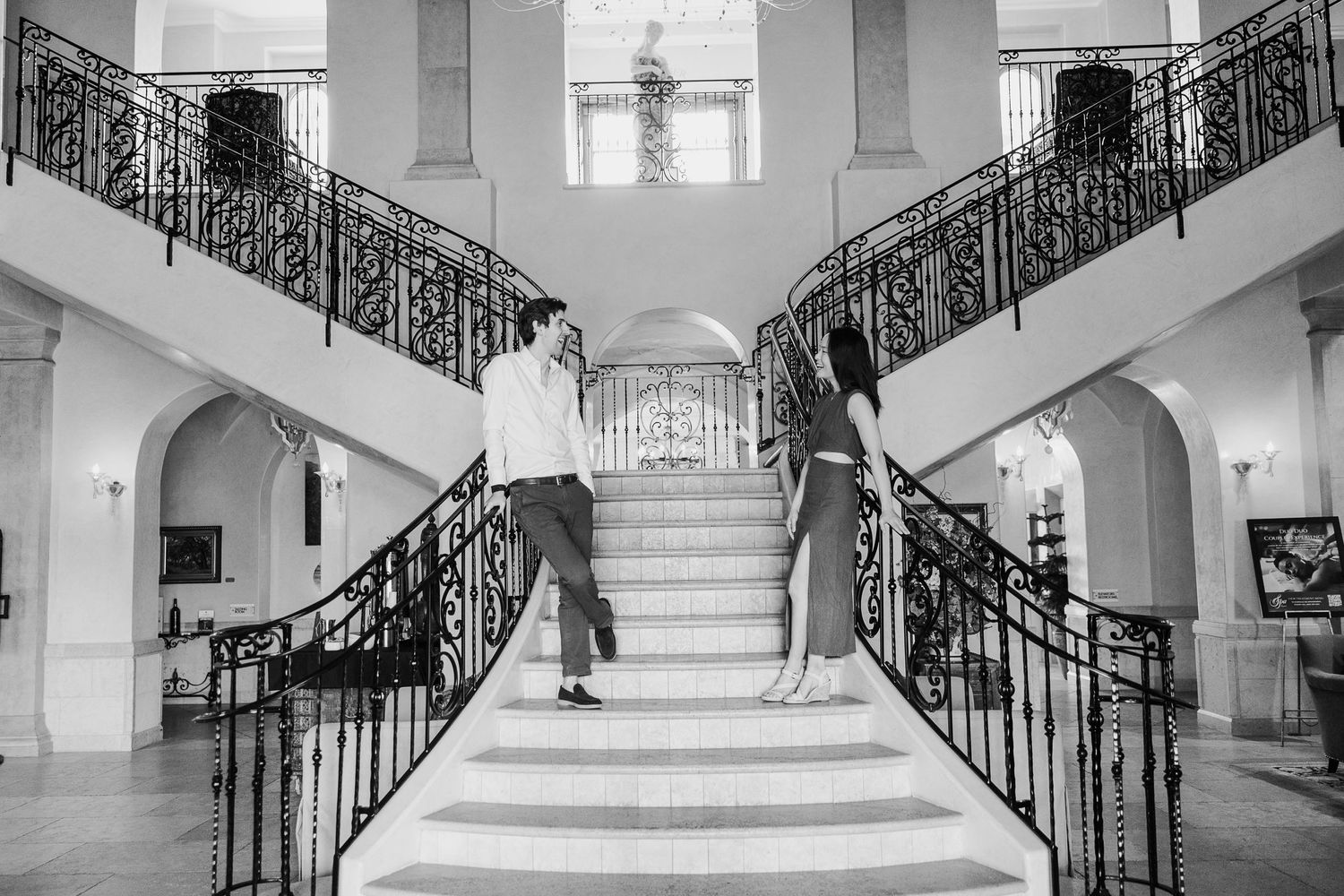 A black and white photo of a couple on opposite sides of an elegant grand staircase.