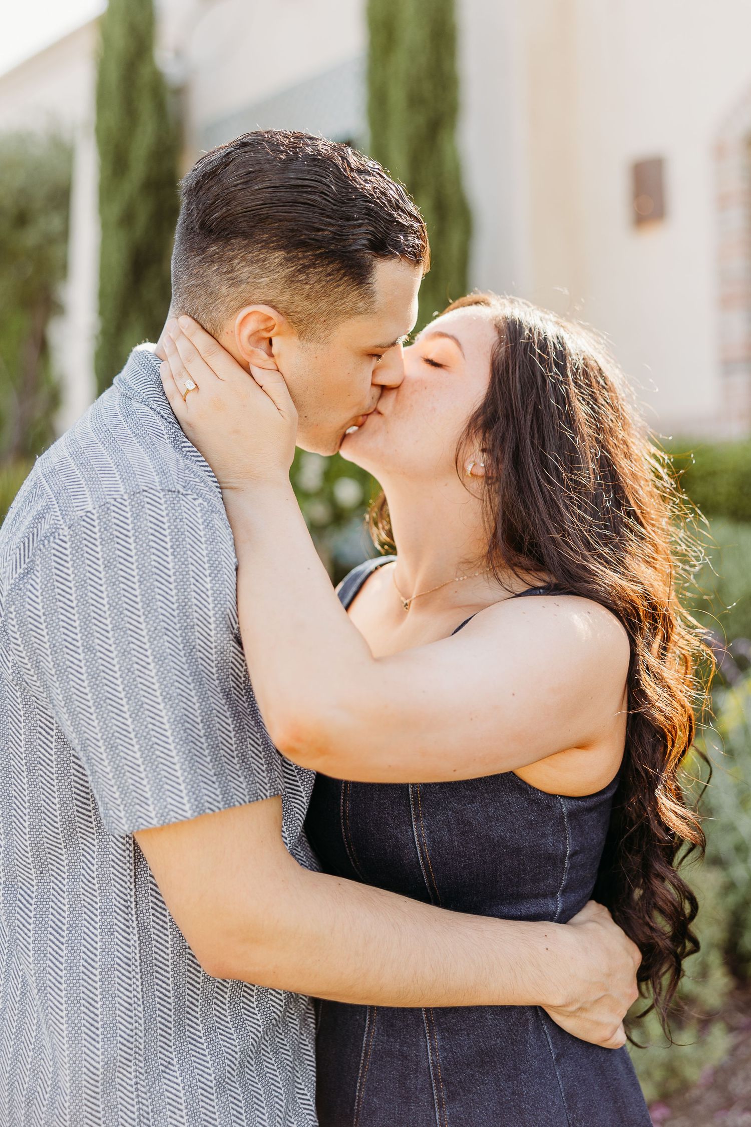 A tender embrace between a couple in a garden setting with cypress trees in the background.