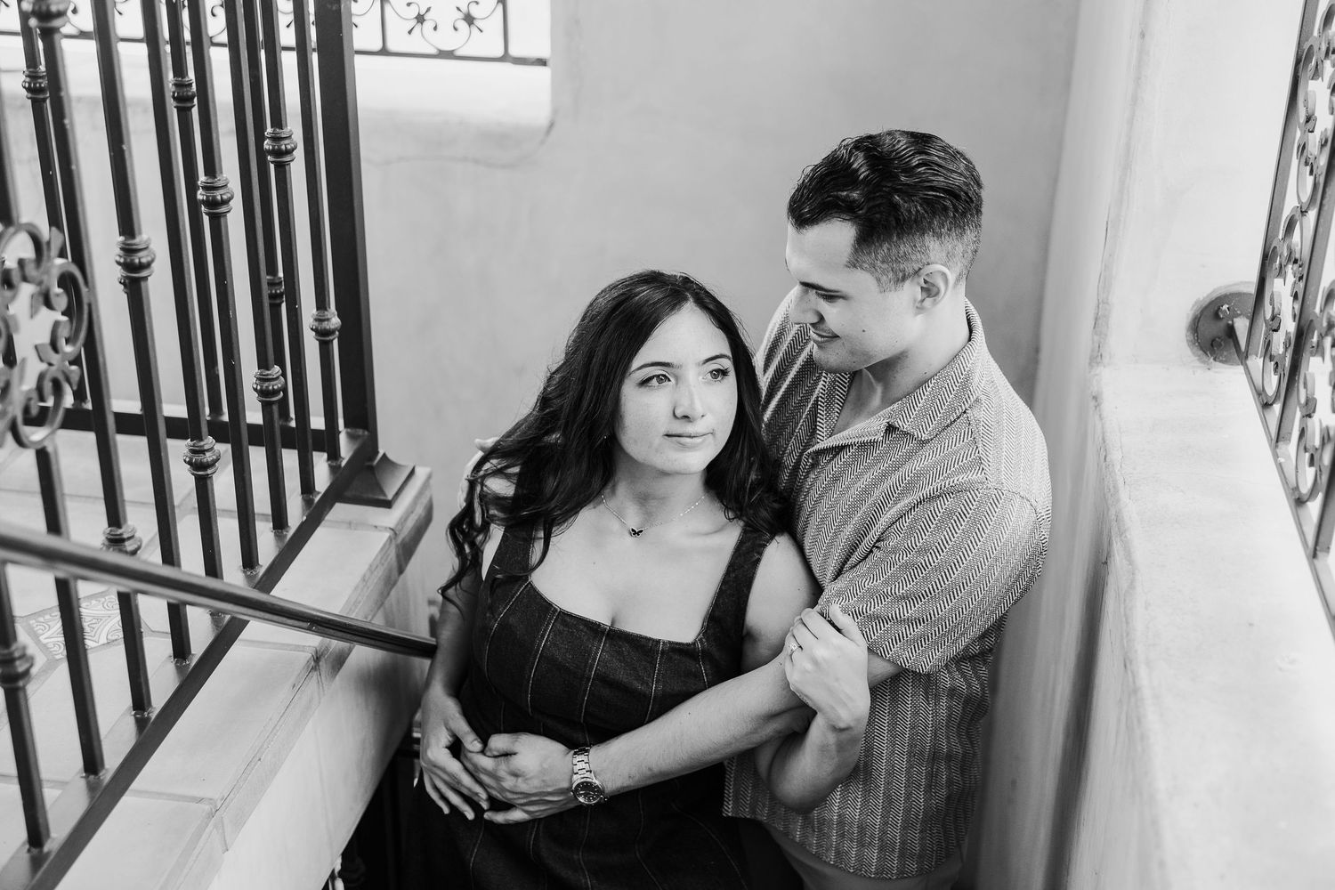 Intimate indoor couple photoshoot in black and white with vertical window frames creating dramatic lighting.