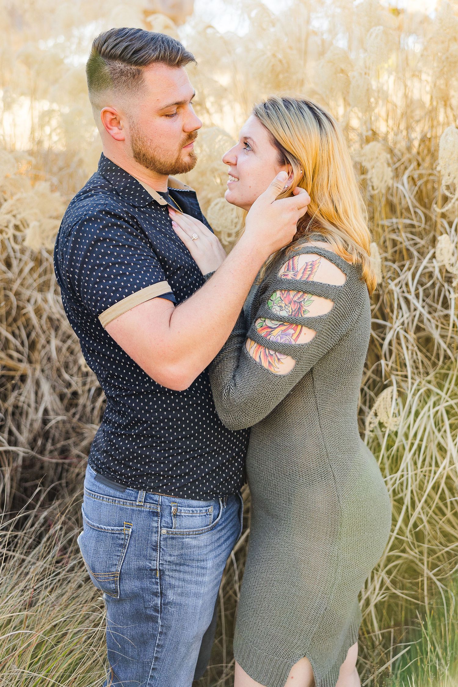 A couple shares a tender moment while standing together in a field of golden grass.