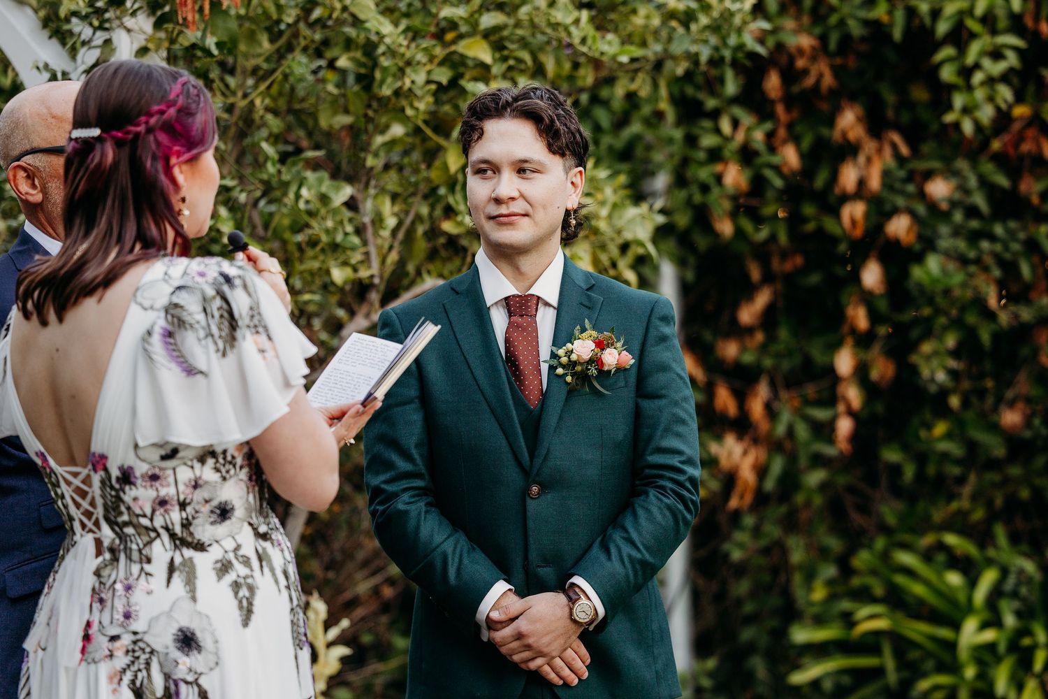Wedding party in formal attire standing outdoors with green foliage in the background.