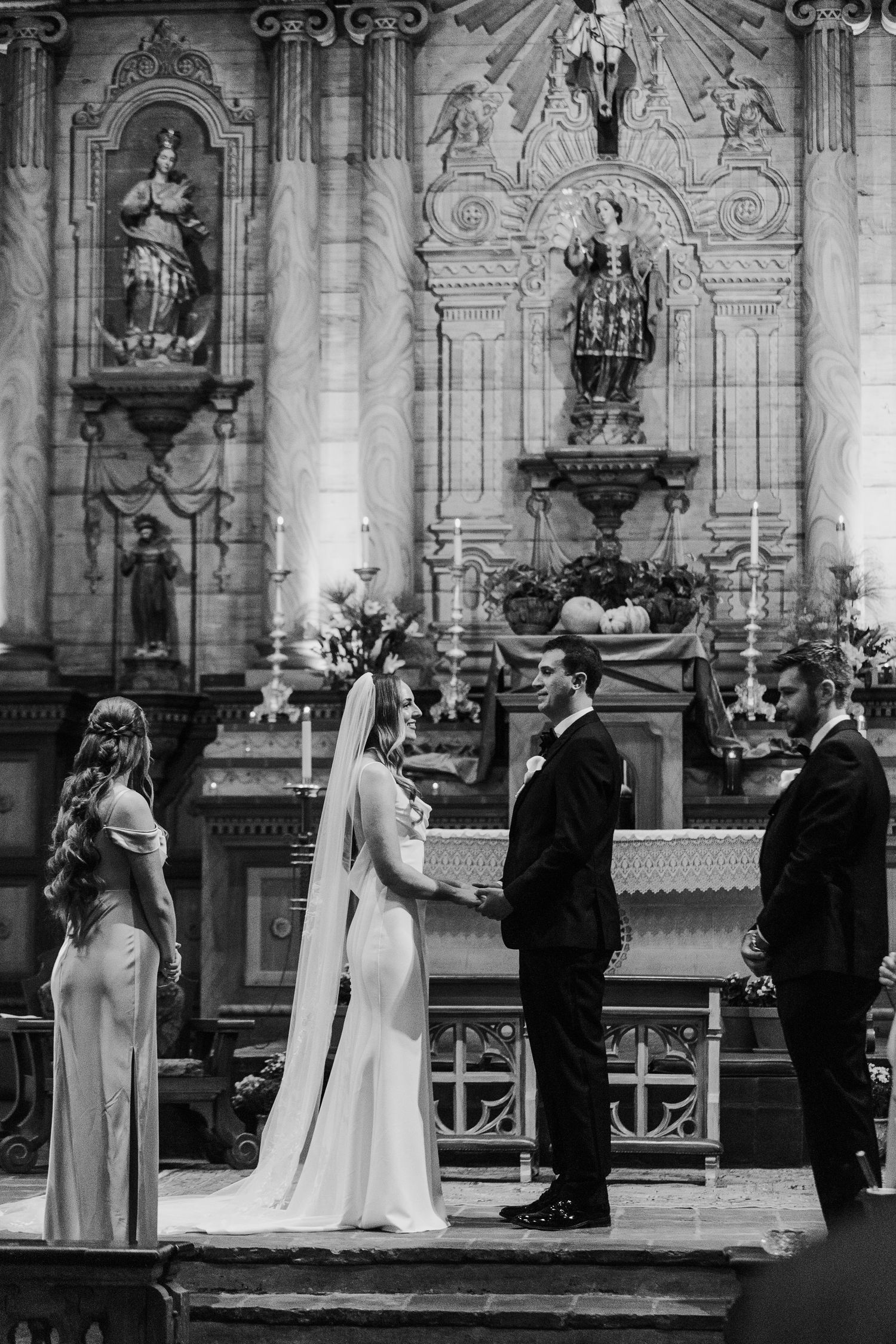 Elegant church wedding ceremony with ornate religious statues and decorative architecture in black and white.