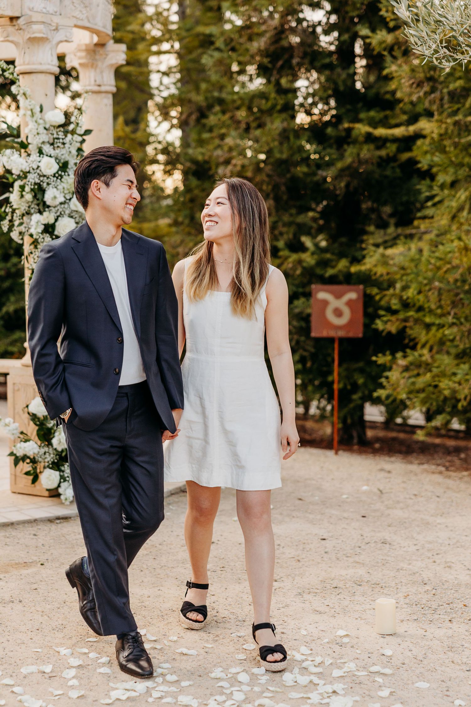 A couple shares a joyful moment while walking together on a garden path with floral decorations.