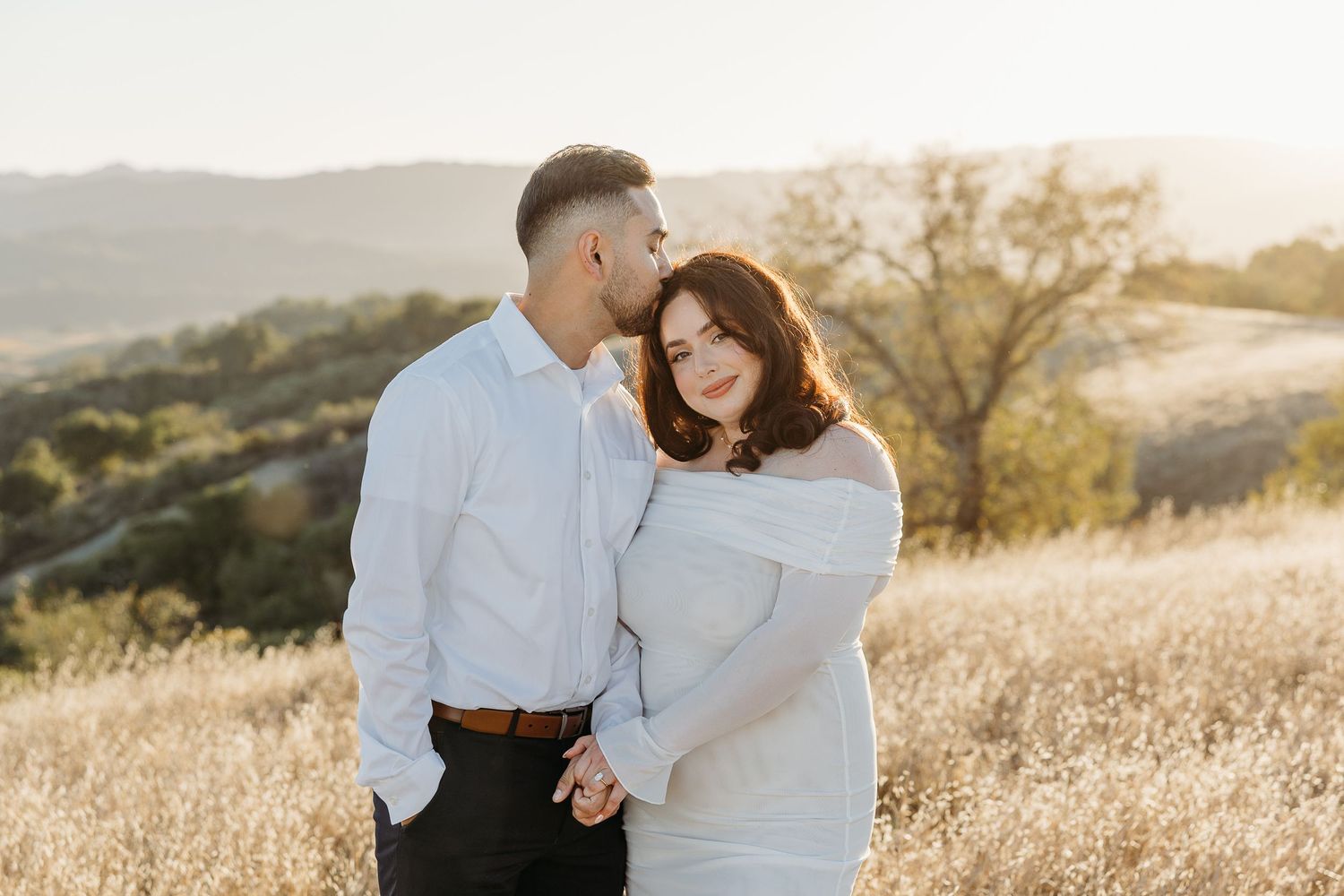 Engagement photos in a golden field during sunset with mountains in the background.