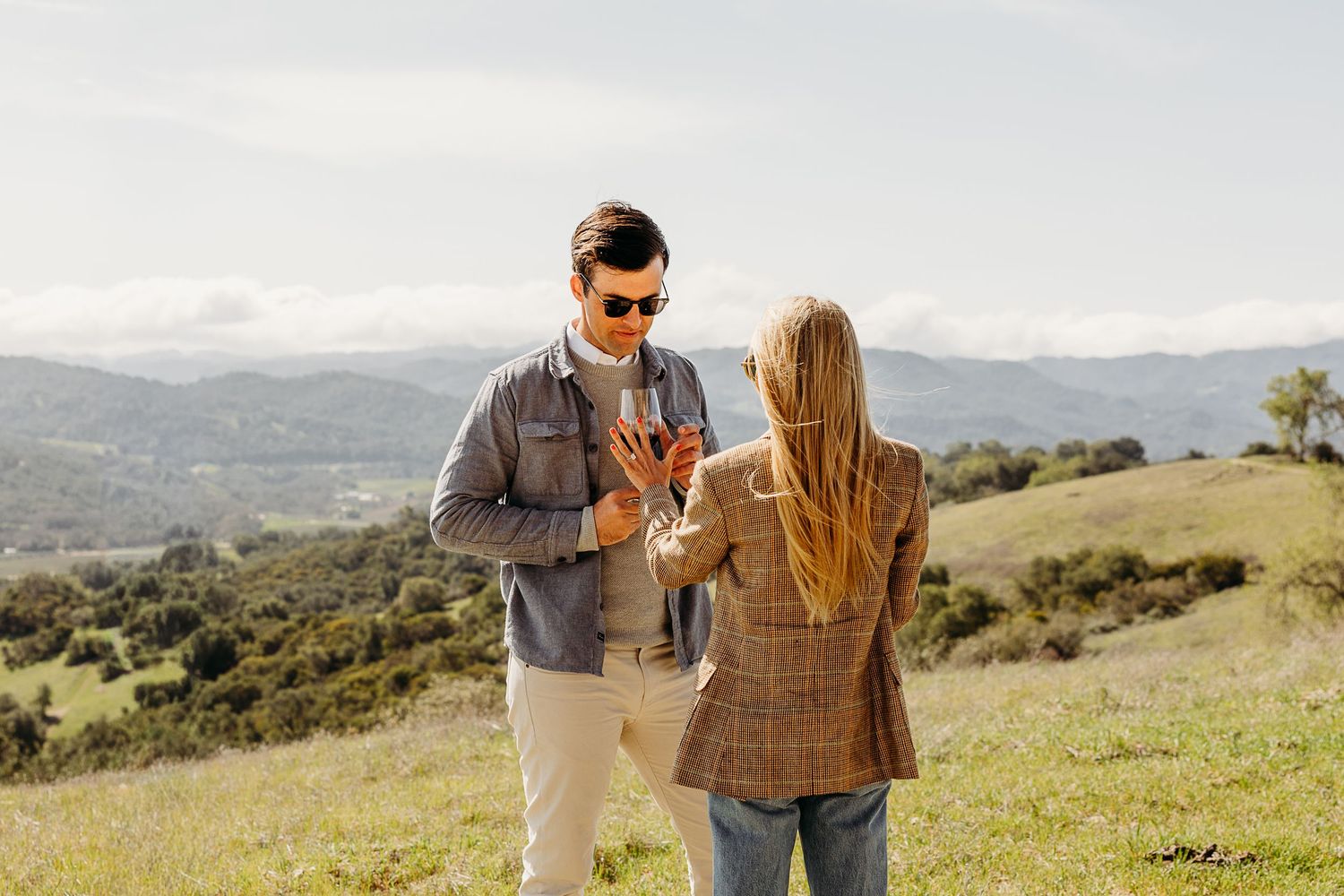 A couple shares a romantic moment on a scenic hilltop overlooking rolling green mountains during golden hour.