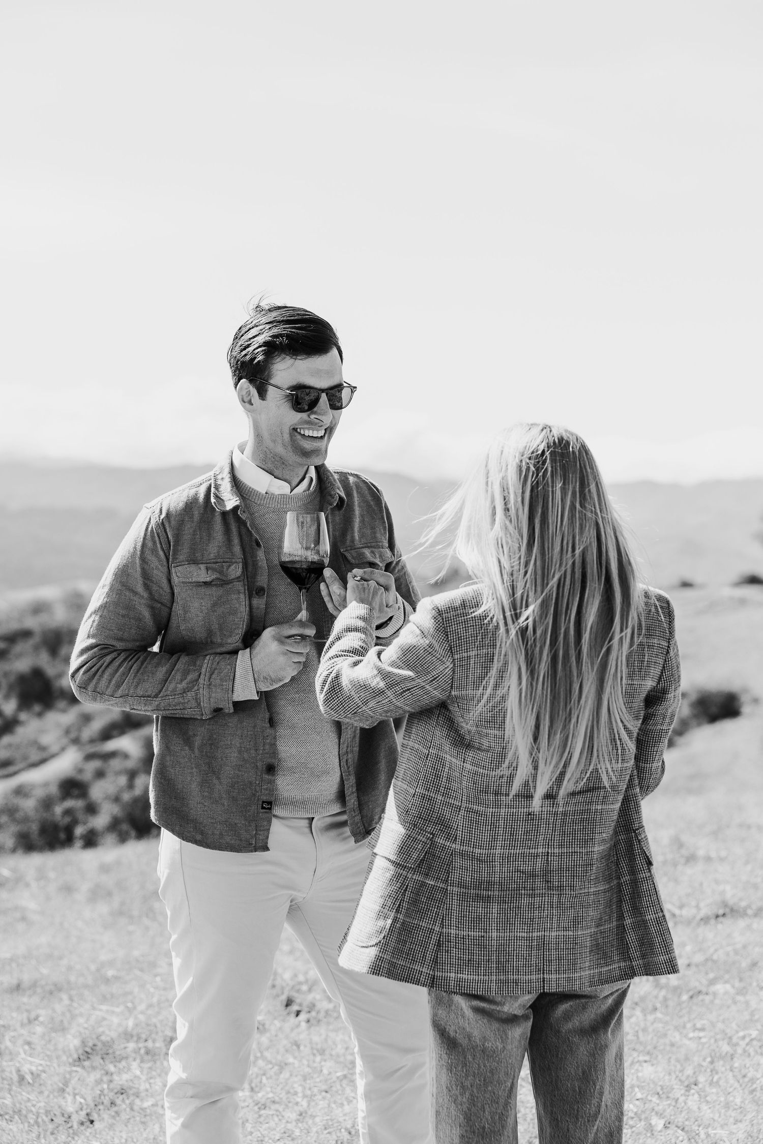 A couple enjoying wine and laughing together on a hilltop overlooking rolling countryside.