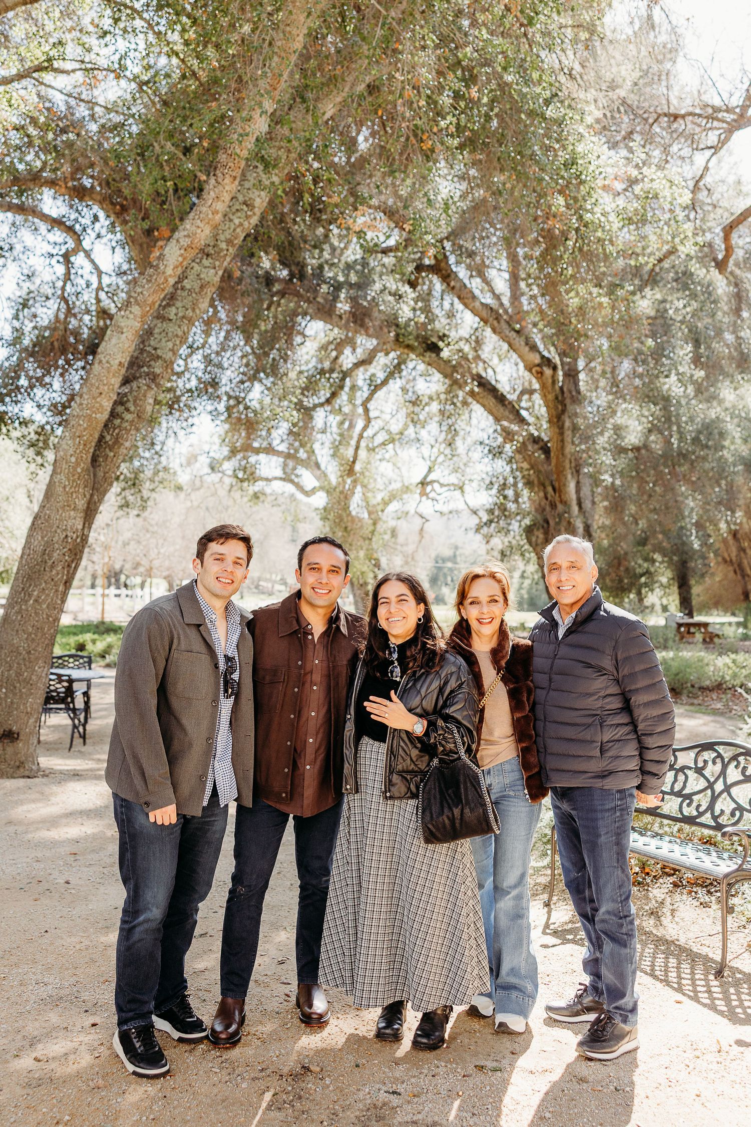 A group of people standing together outdoors under olive trees on a sunny day.