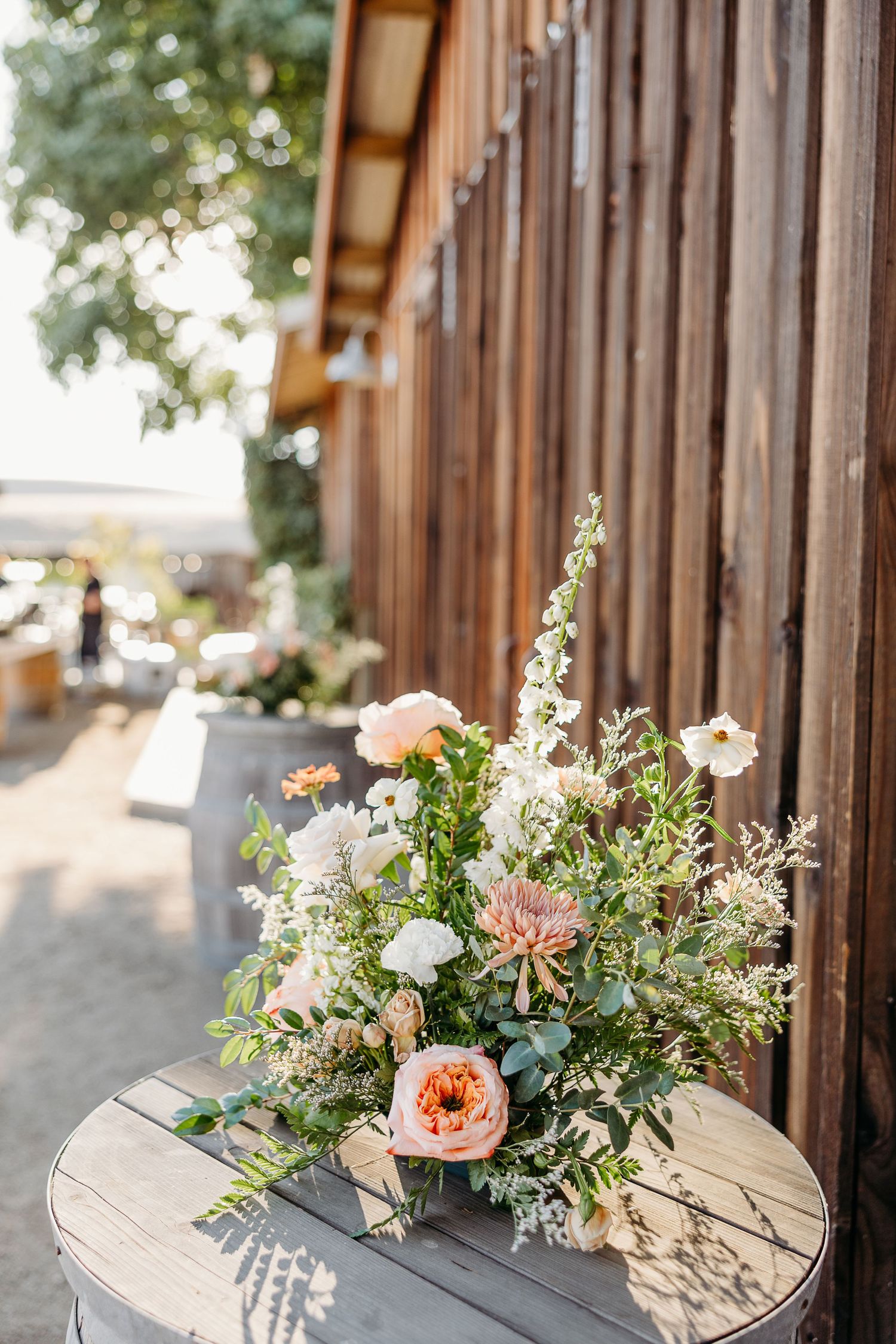 Delicate floral centerpieces with coral and white blooms arranged on rustic wooden surfaces at a wedding venue.