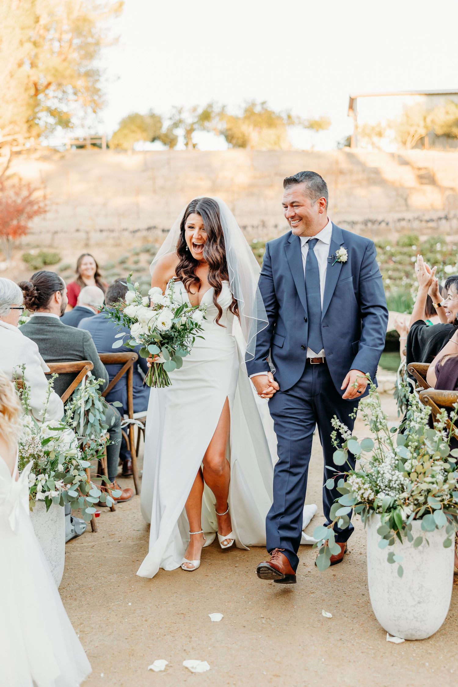 Wedding guests mingle at an outdoor reception with rustic decor and floral arrangements.