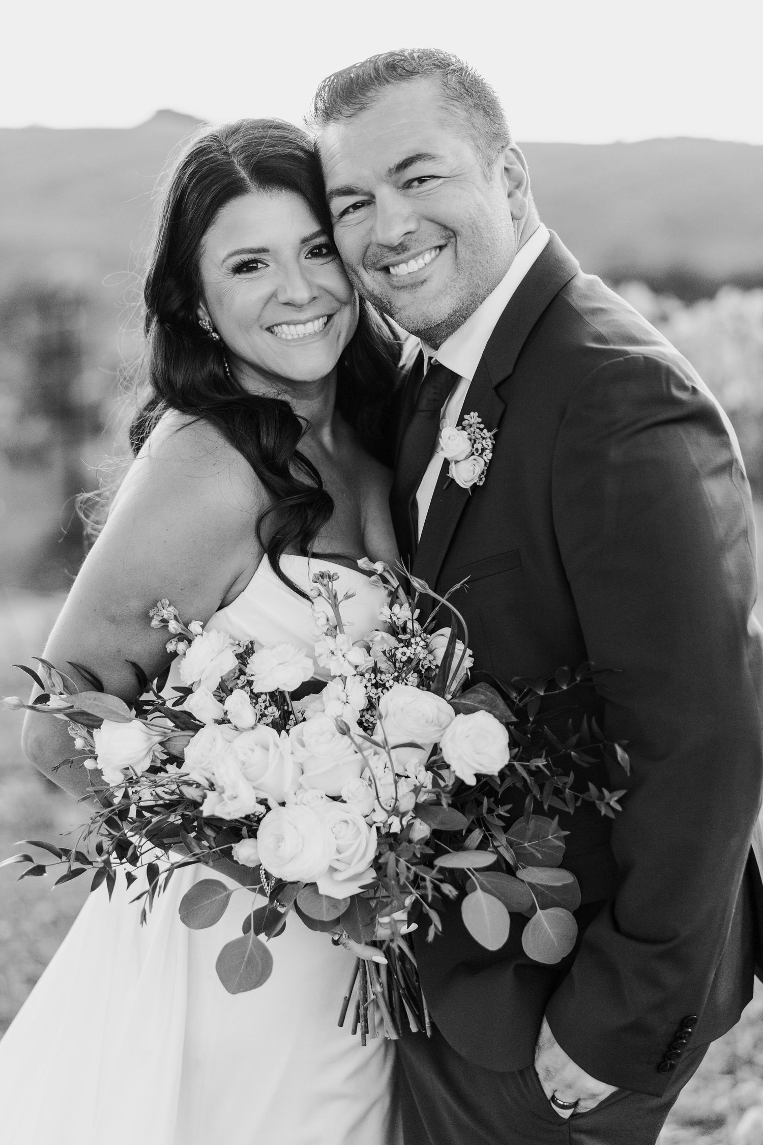 Black and white wedding portraits showing a happy couple with a lush floral bouquet against a desert backdrop.