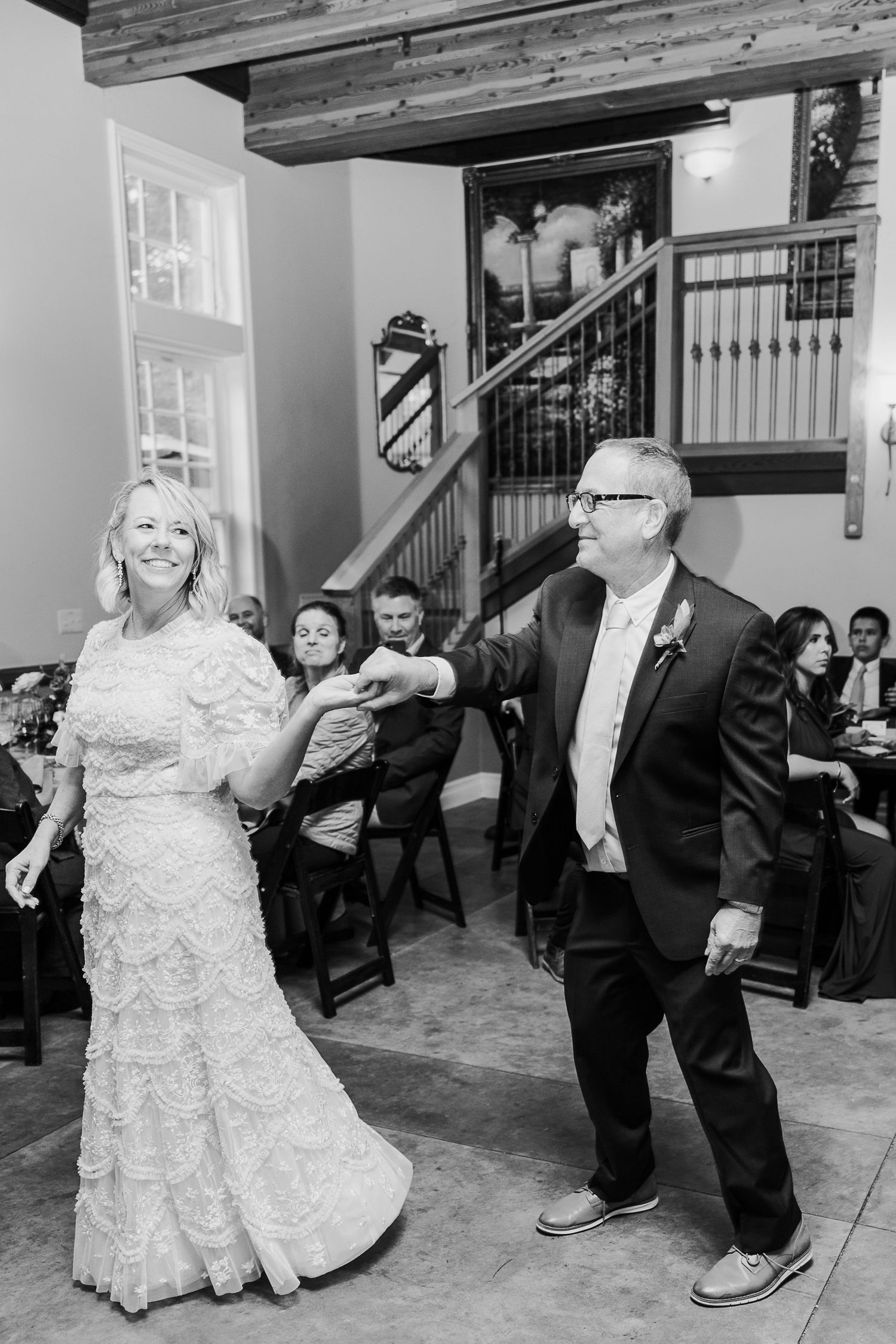 A couple dancing and celebrating at their wedding reception in a rustic venue with wooden beams.