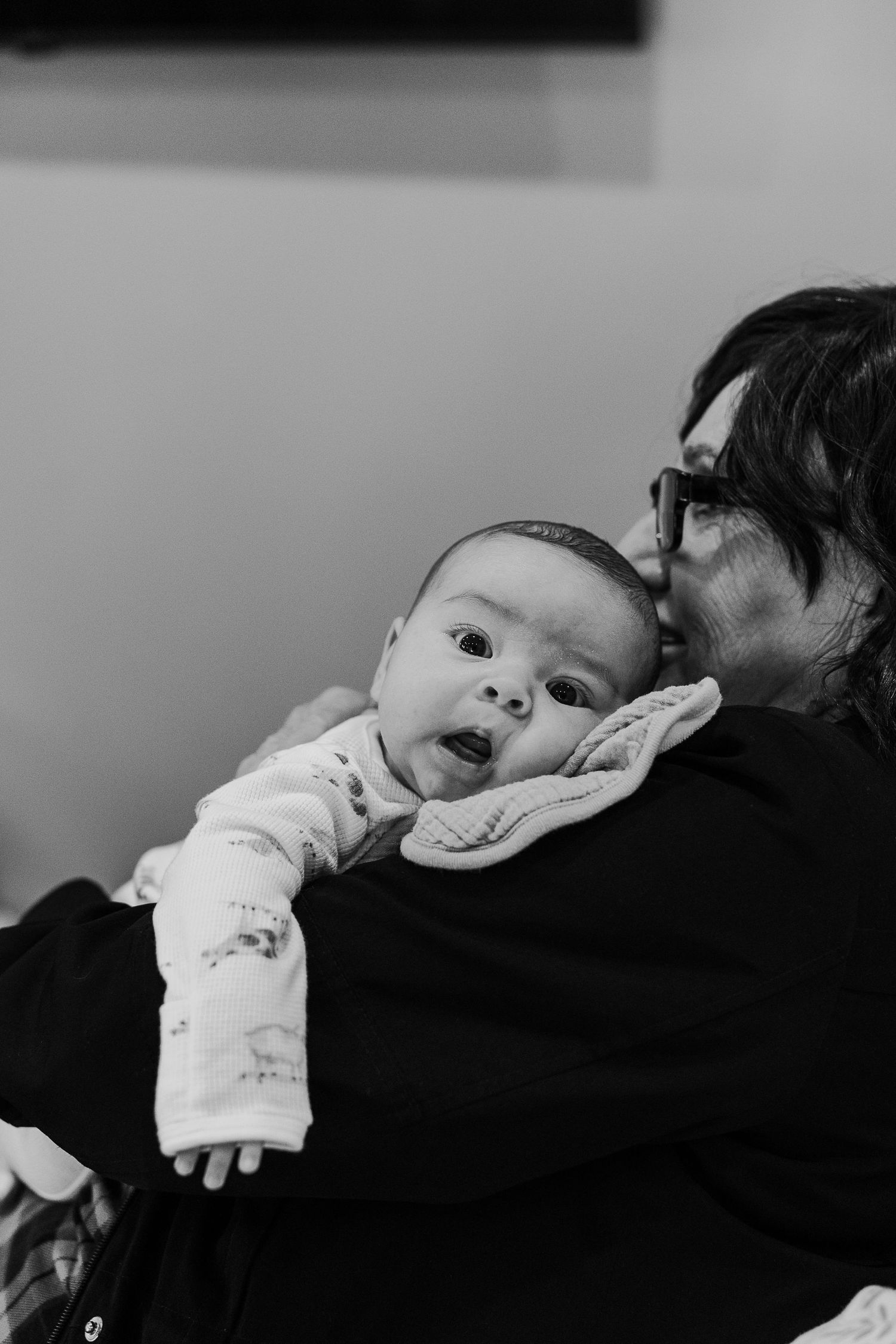 Black and white photo of a baby in a white onesie laying on someone wearing dark clothing.