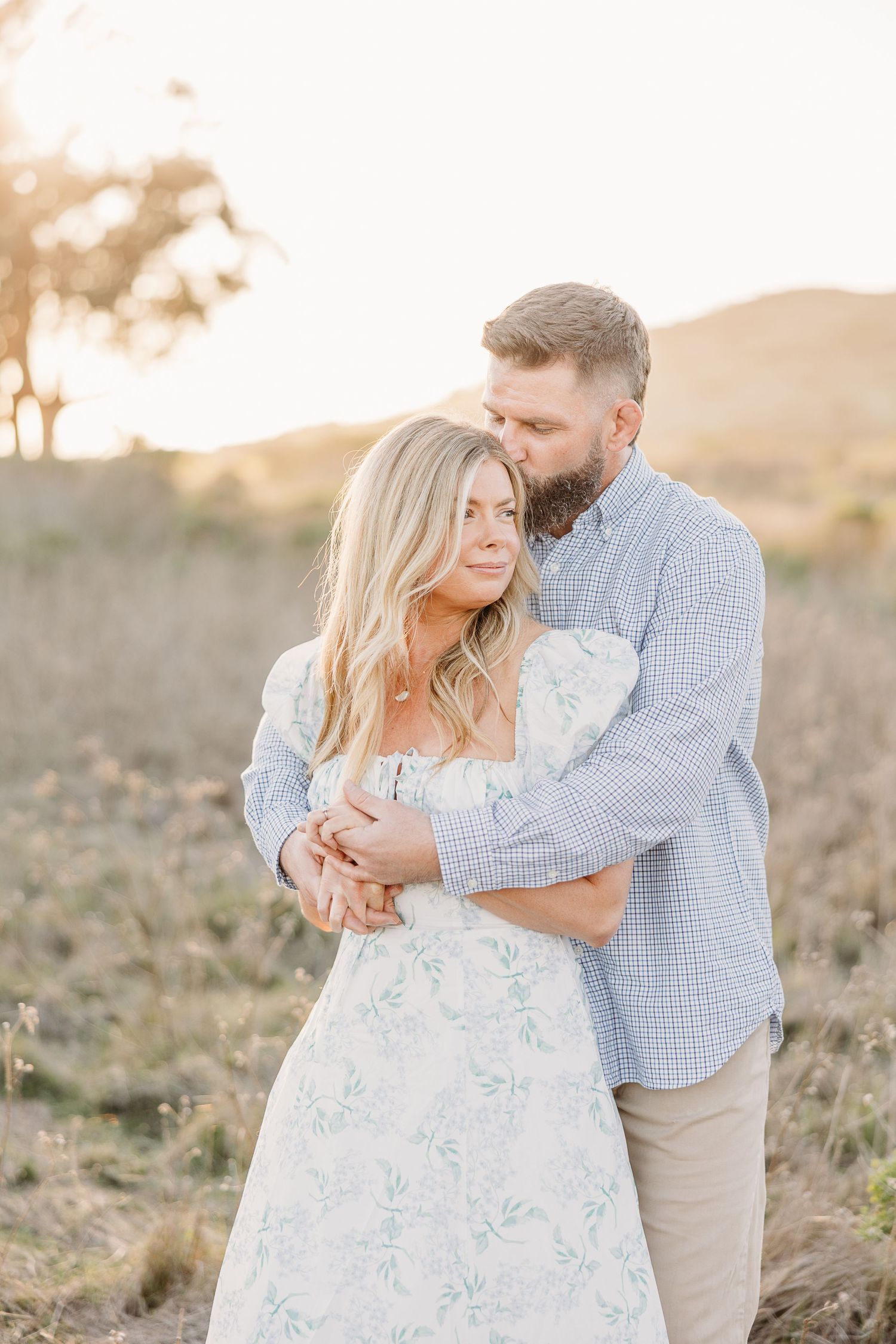 Romantic couple embracing during sunset engagement photo session in golden field.